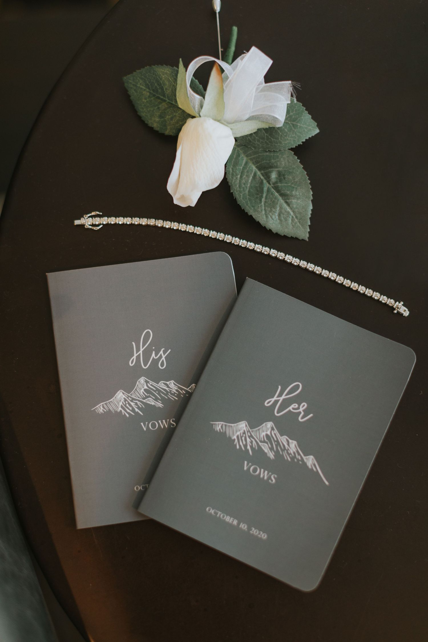 Gray wedding vow books with mountain designs displayed with white floral accents.