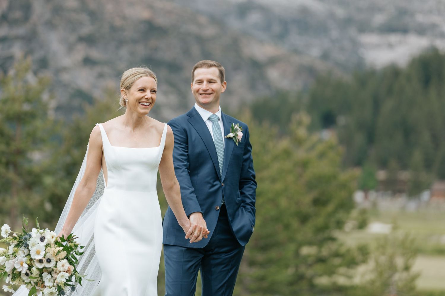 Newlyweds share a candid moment against stunning mountain scenery.