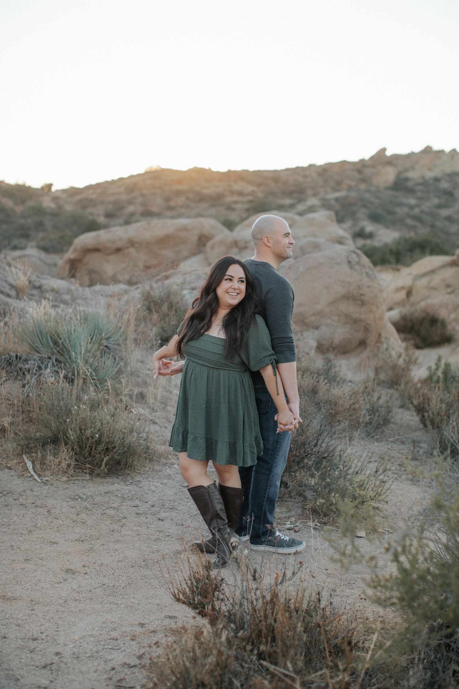 A couple plays and poses together among desert brush and rocks.