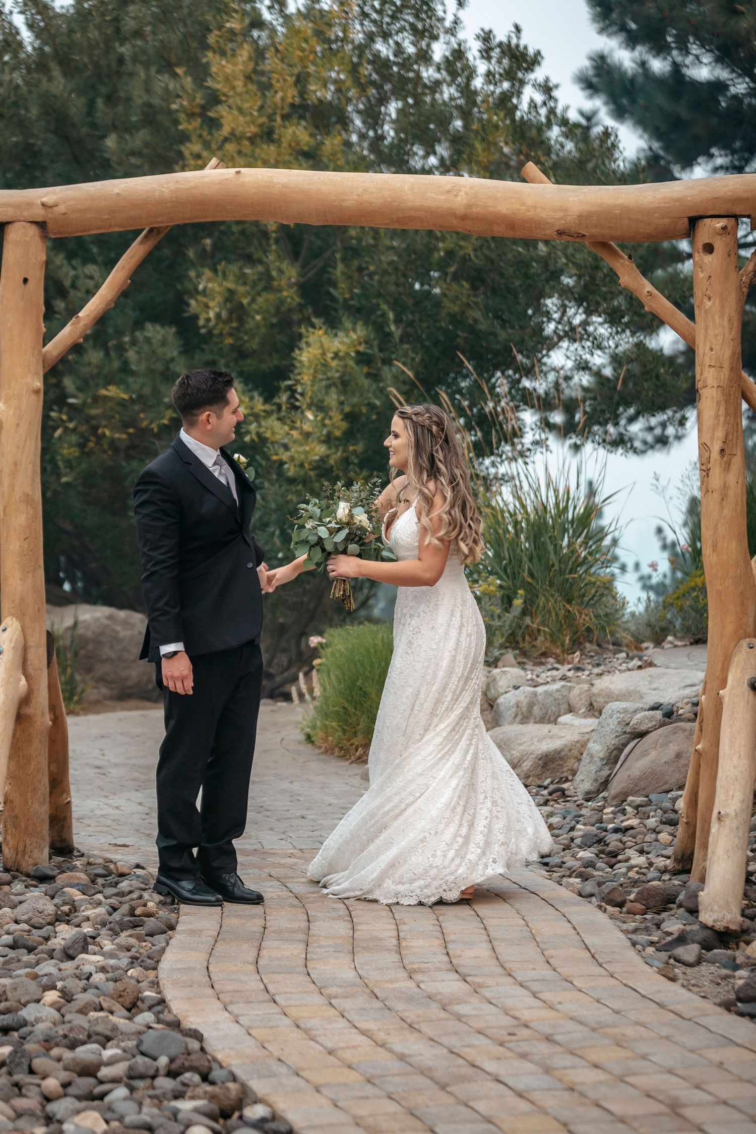 Couple sharing a moment under rustic wooden arch during outdoor wedding ceremony.