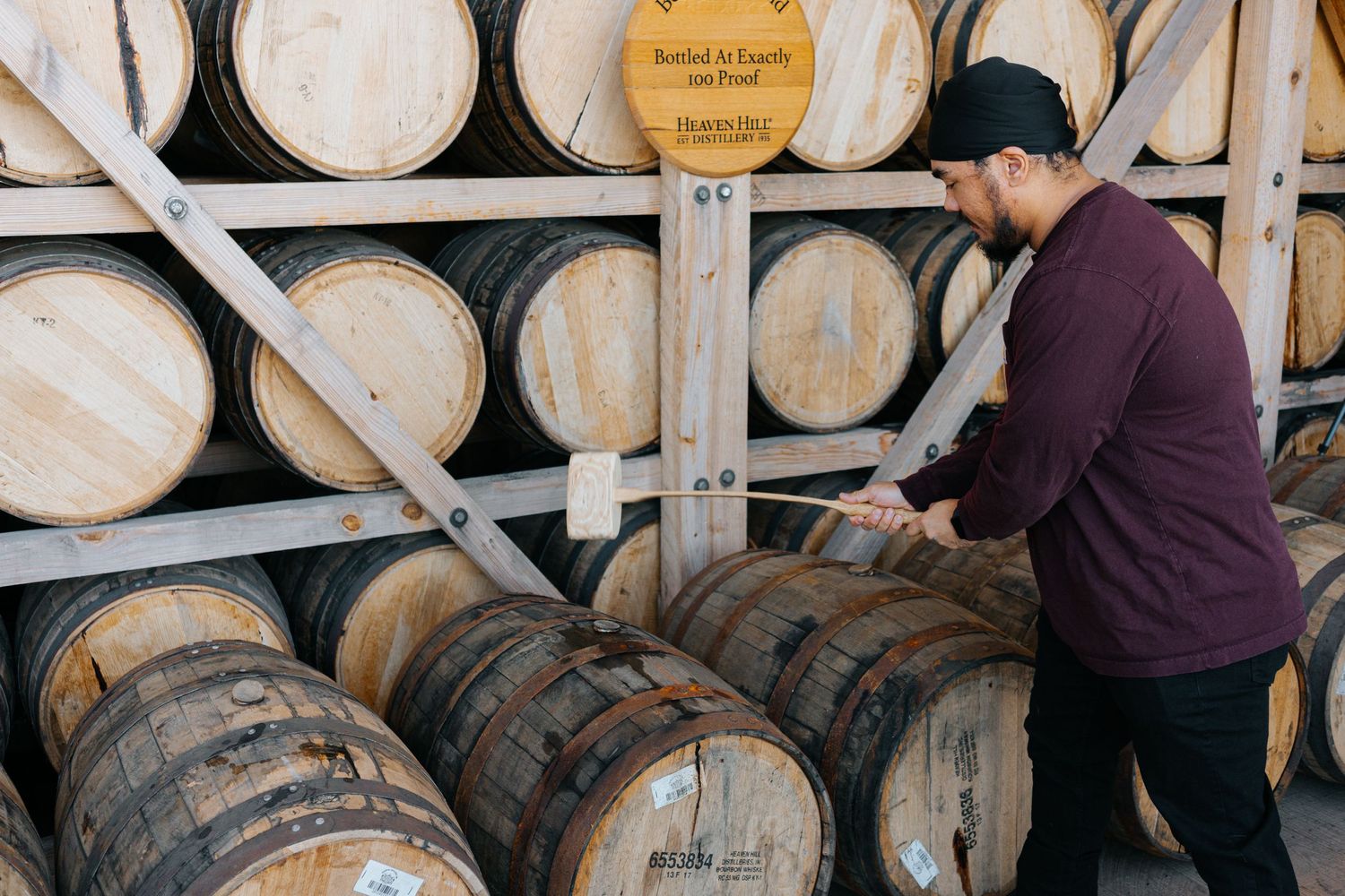 Workers checking and marking bourbon barrels in a warehouse rack system.