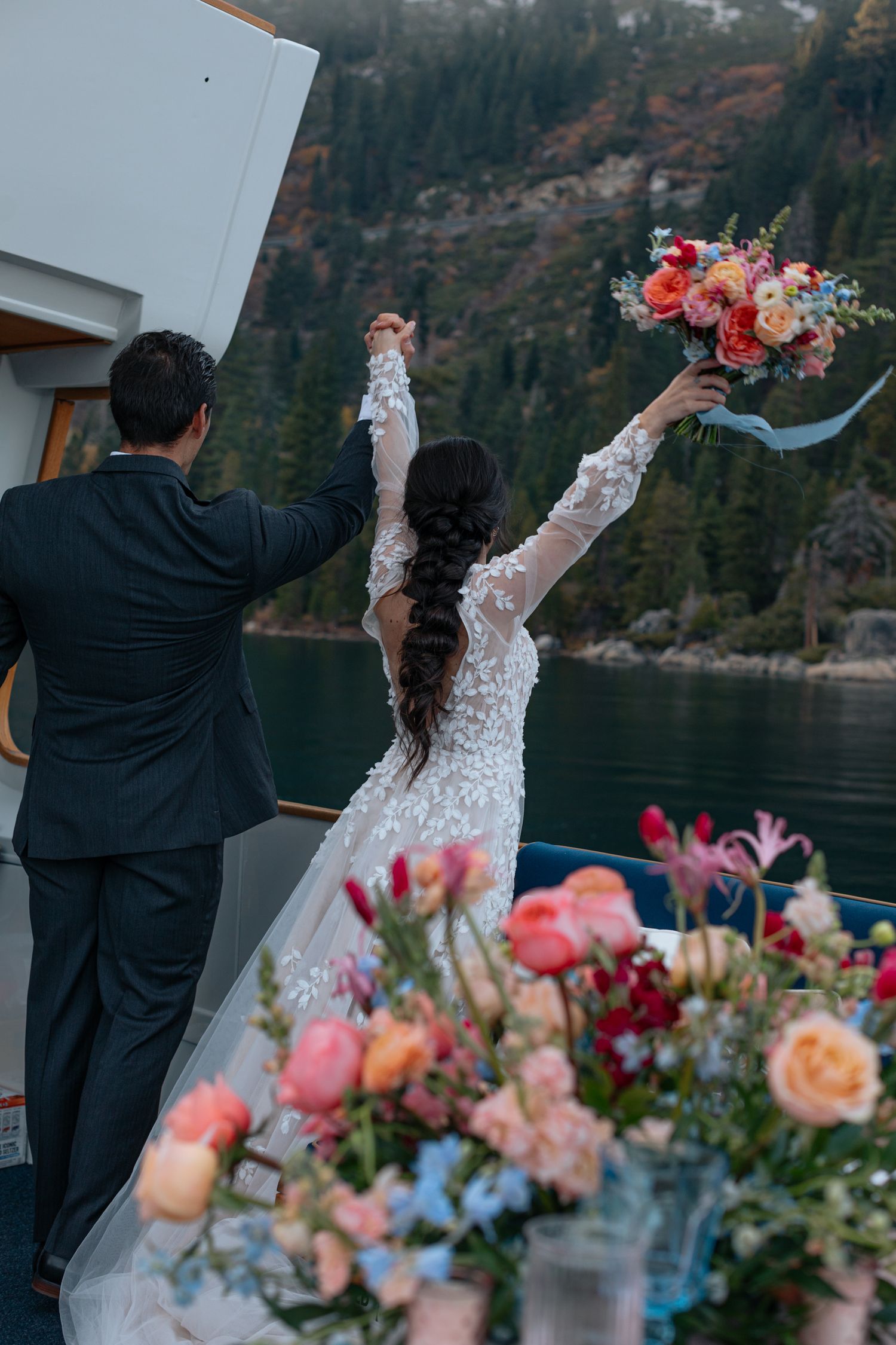 Newlyweds celebrate on a boat deck with raised arms and beautiful floral arrangements.