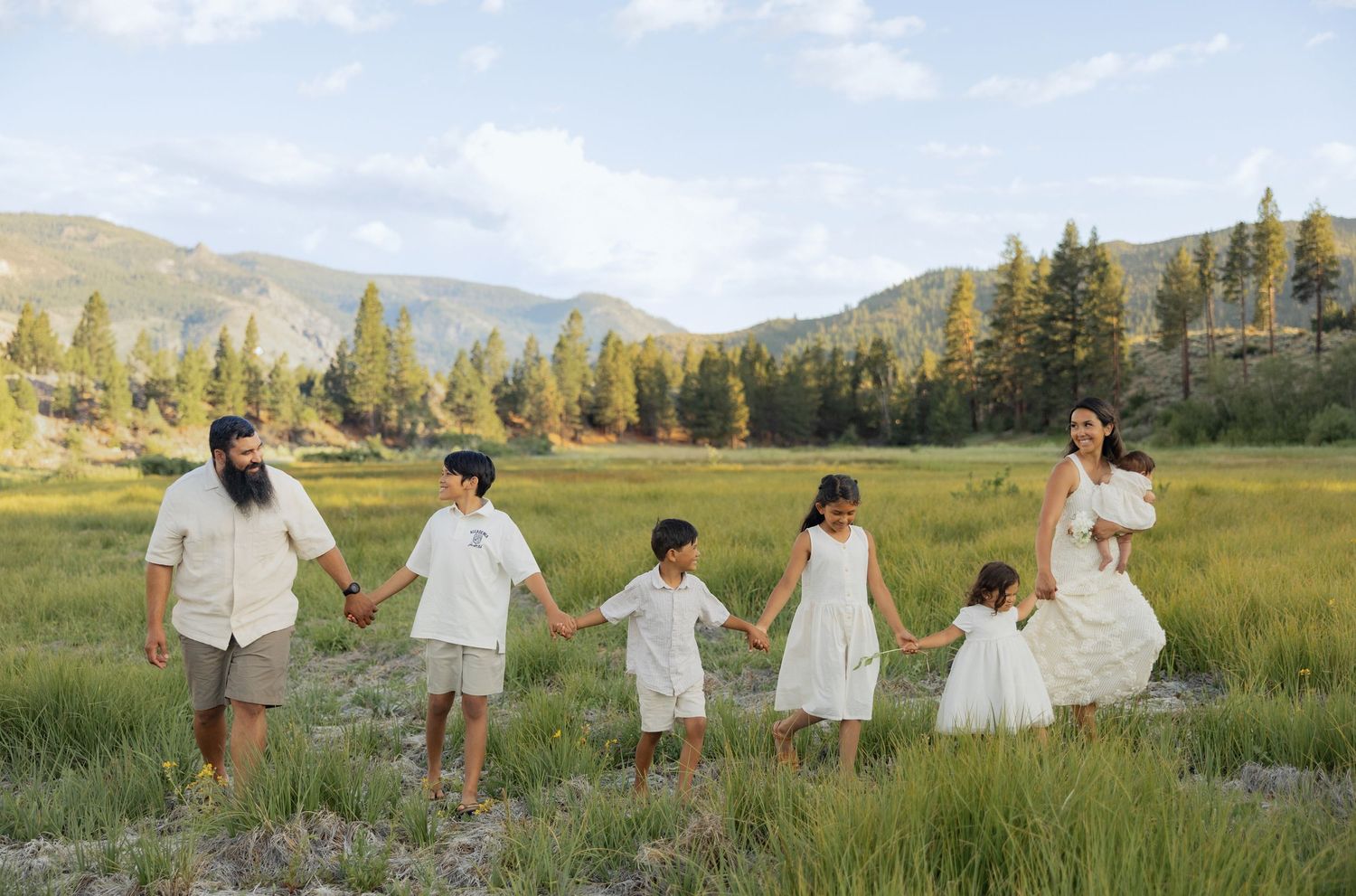 Family holding hands while walking through a scenic mountain meadow at sunset.