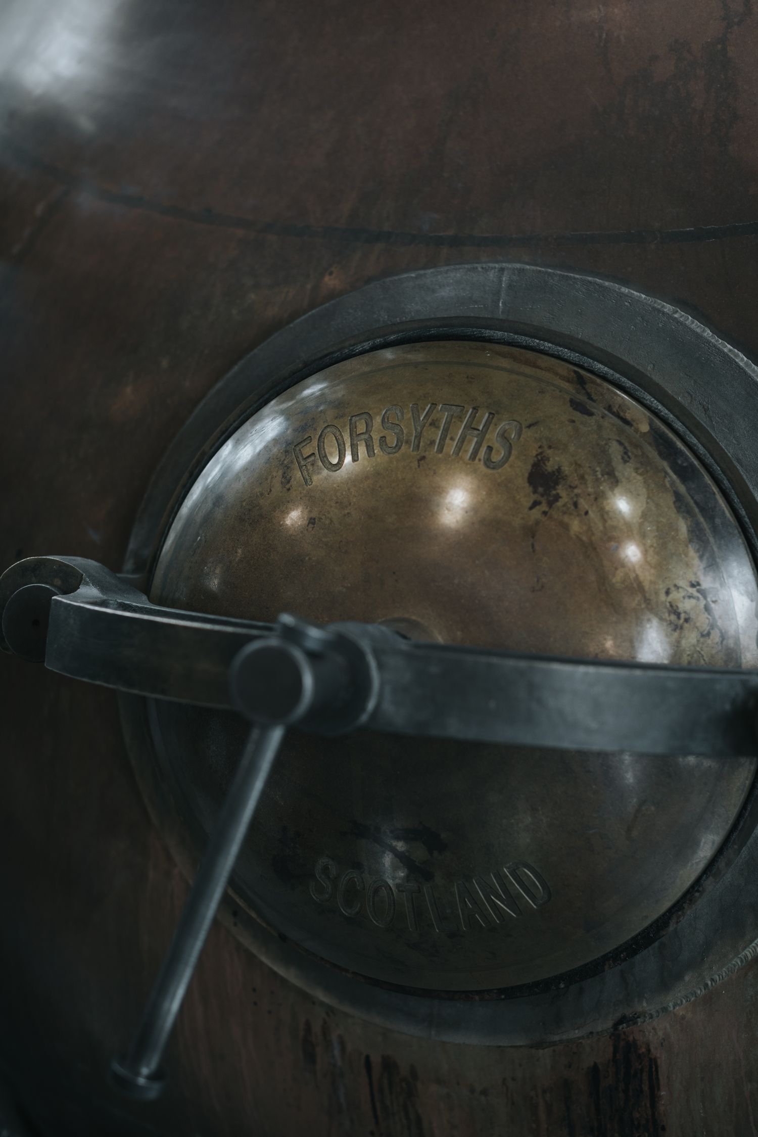 Close-up of vintage copper still door with dark patina and metallic details.