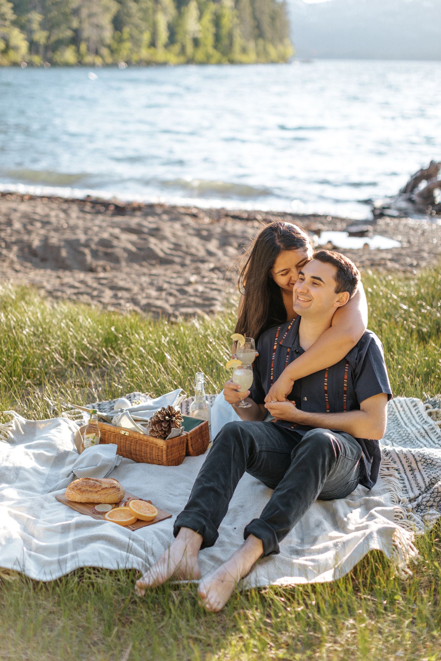 Couple enjoying a romantic picnic by the water's edge on a blanket with a wicker basket.