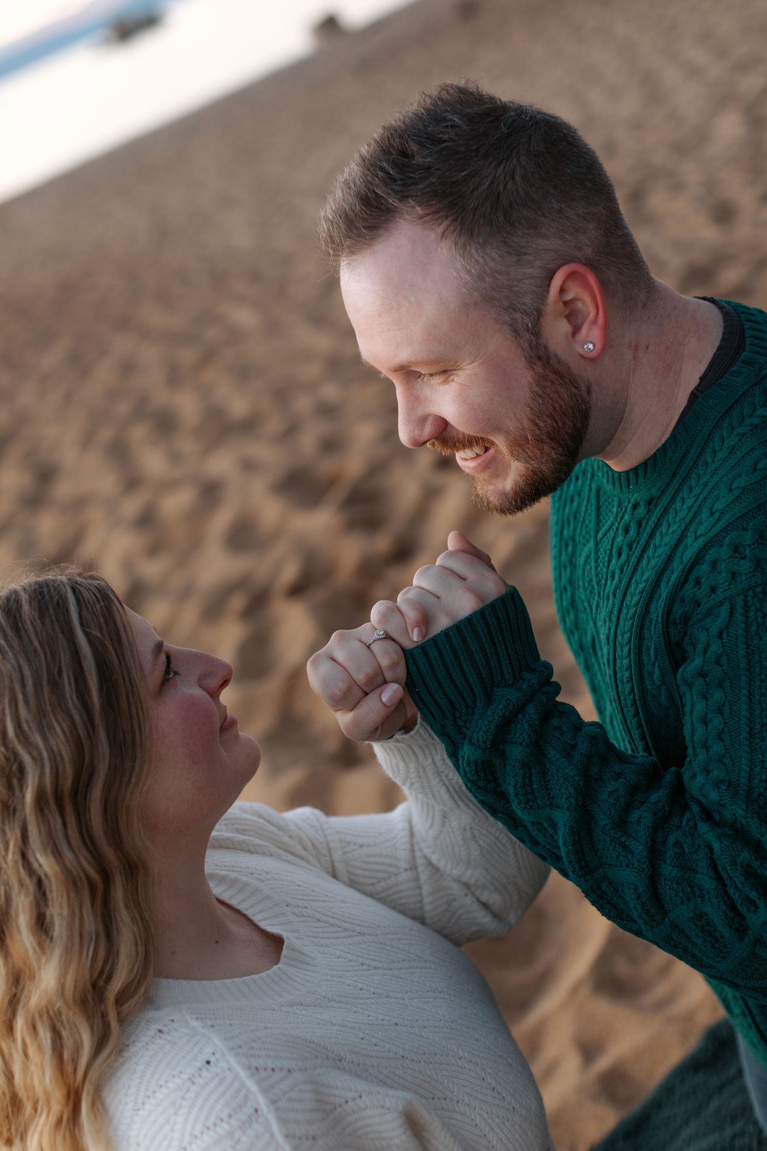 Couple shares playful moment on beach during sunset engagement session.