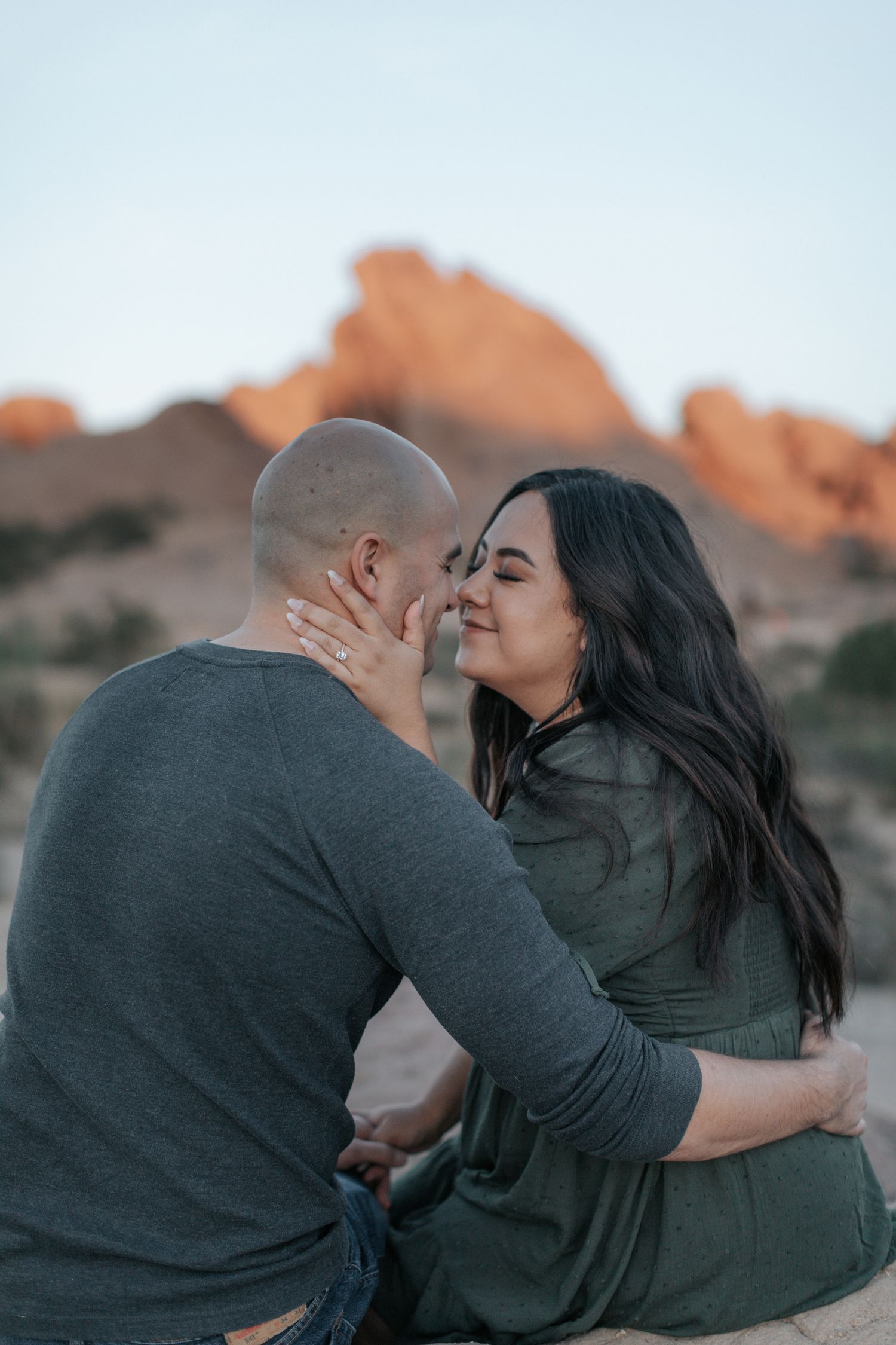 Couple sharing intimate moments against a desert mountain backdrop during sunset photoshoot.