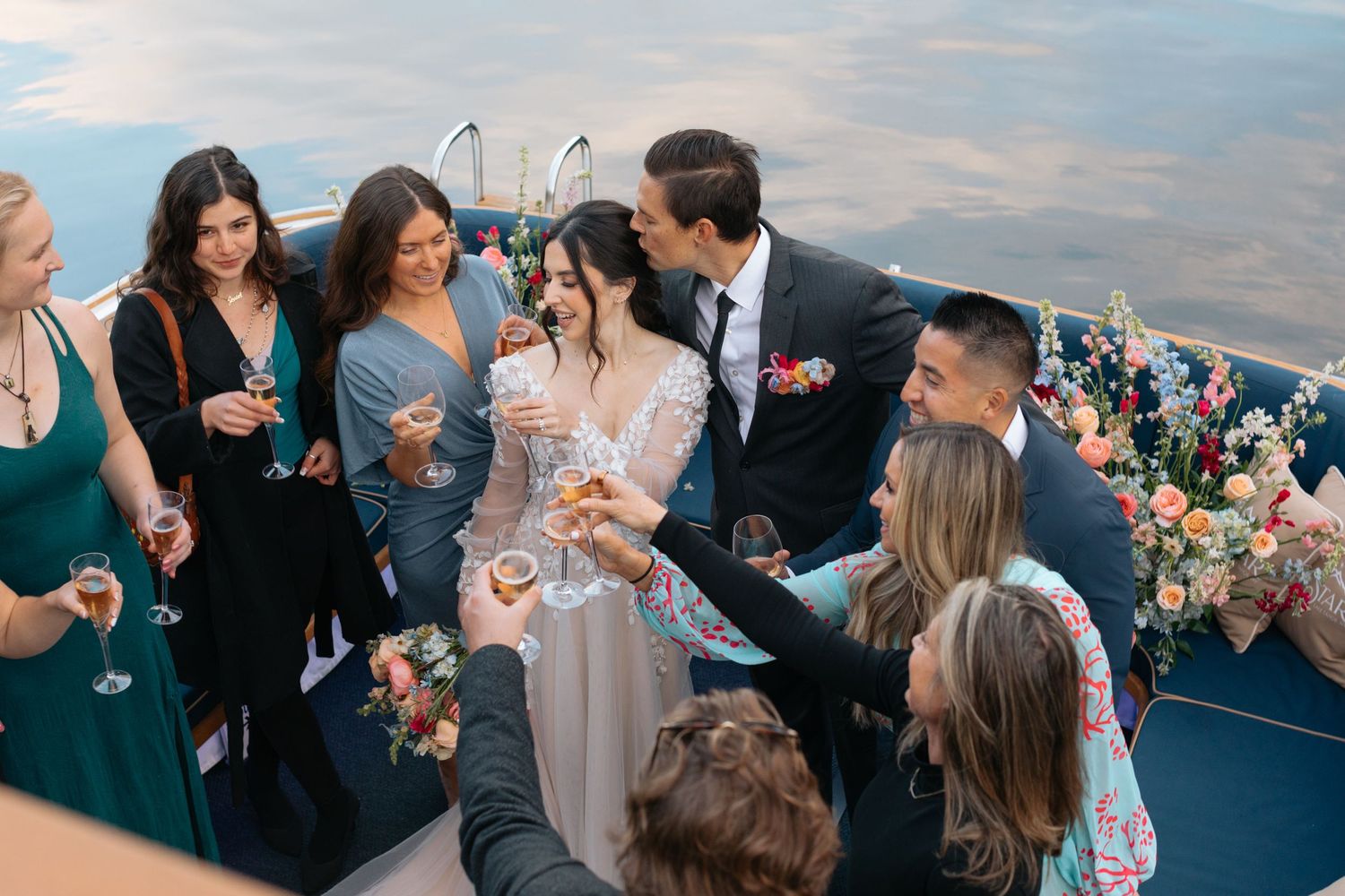 Wedding guests mingling and celebrating on boat deck at sunset.