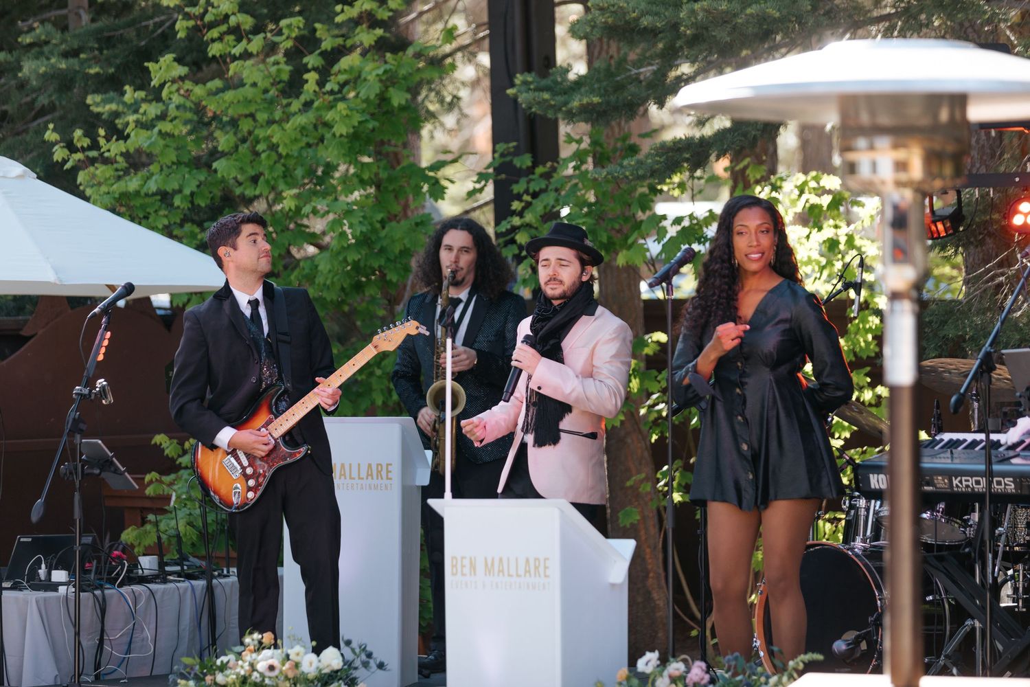 Live band performs at an outdoor wedding reception with white decor and floral arrangements.