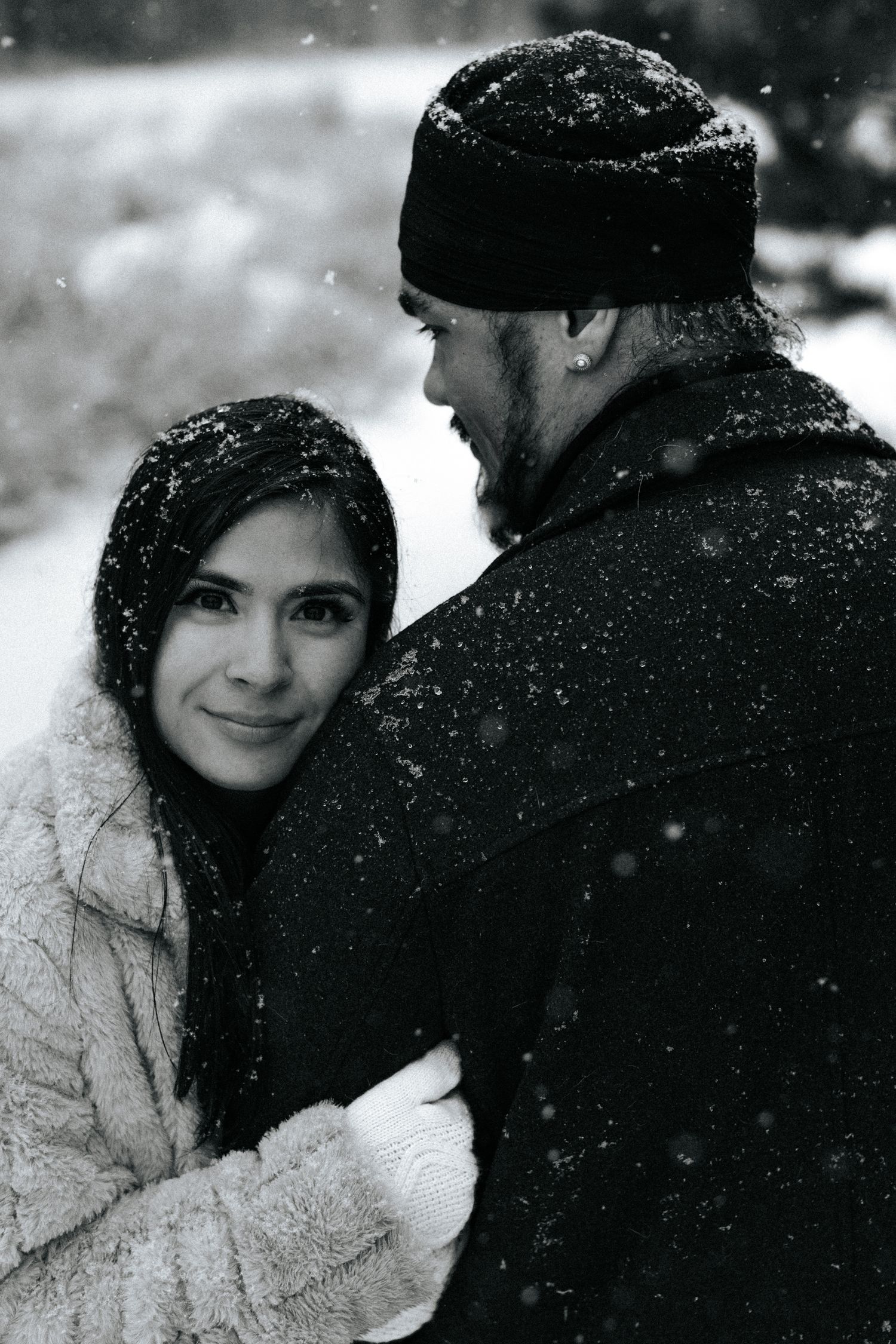 Intimate winter portrait of a couple in the snow with evergreen trees in background.