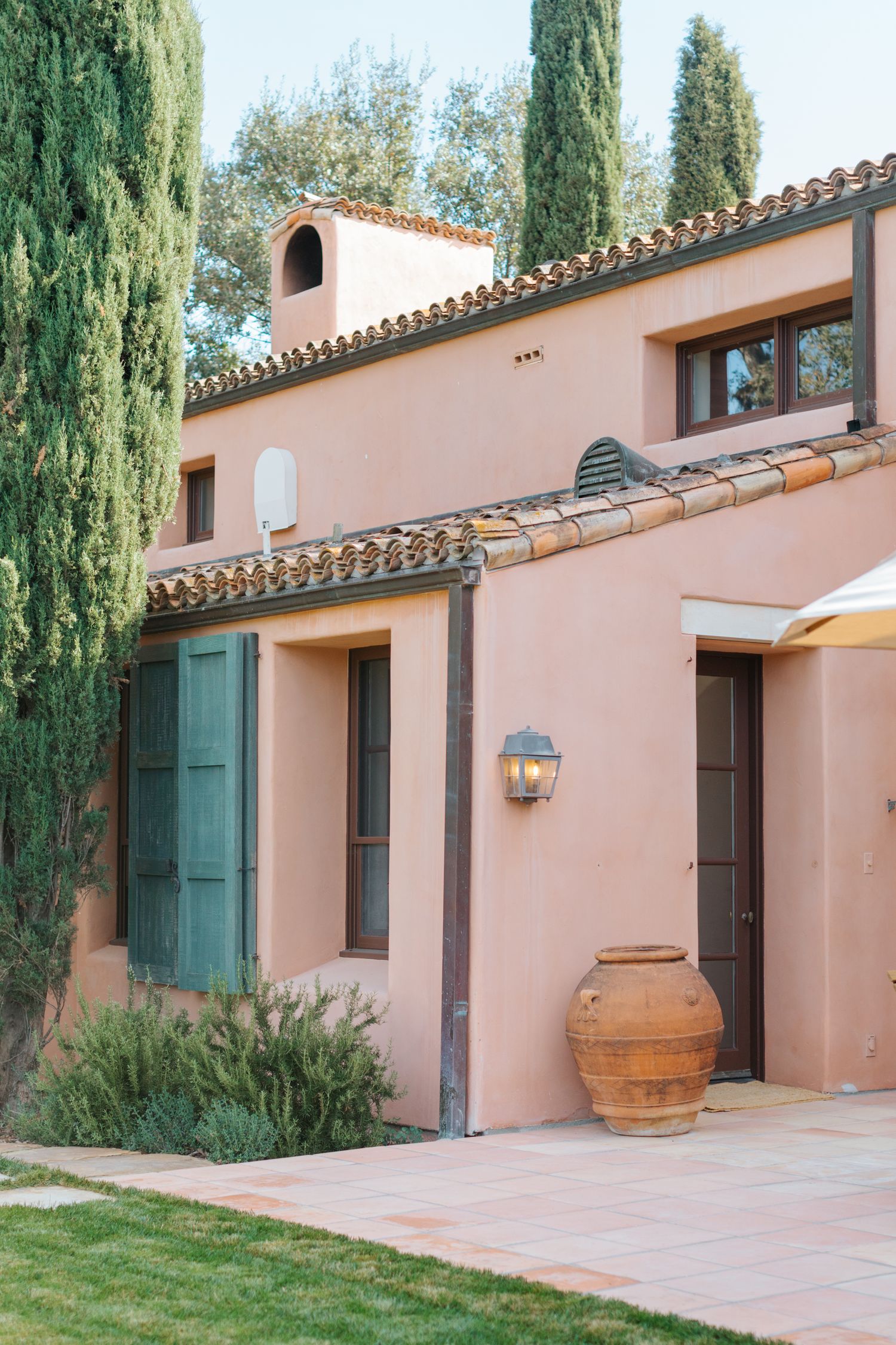 Mediterranean style villa exterior with peach stucco walls, green shutters and tall cypress trees.