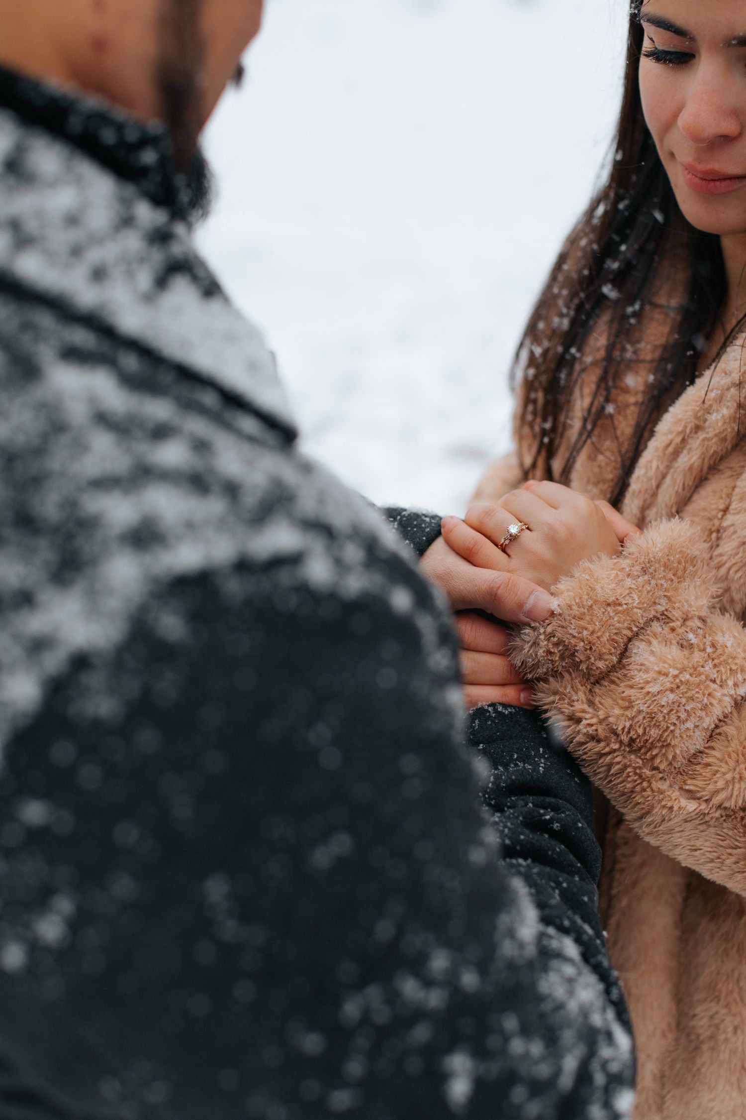 Close-up of hands wearing winter gloves showing an engagement ring in the snow.