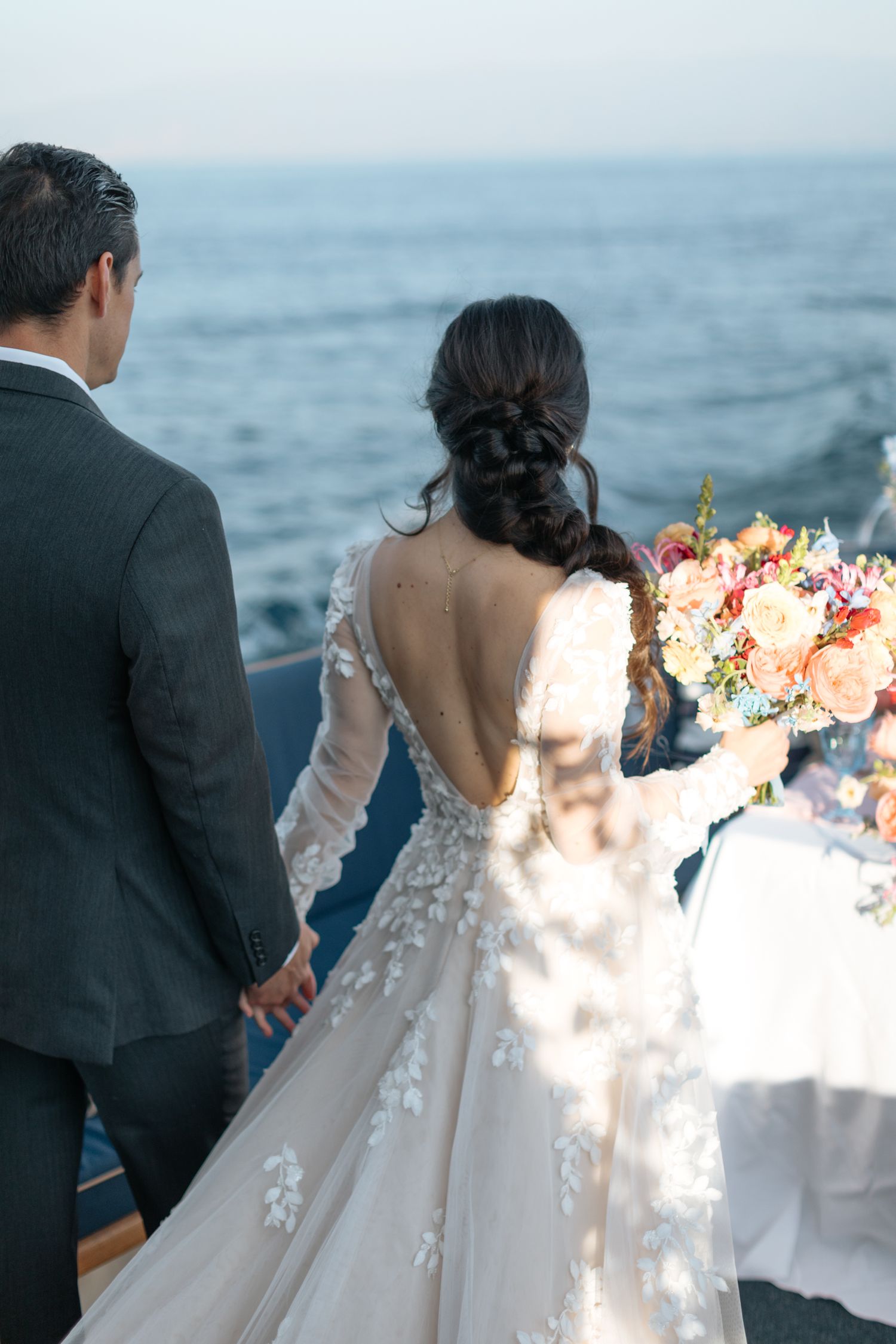 Wedding couple standing by elegantly decorated table on boat with ocean view.