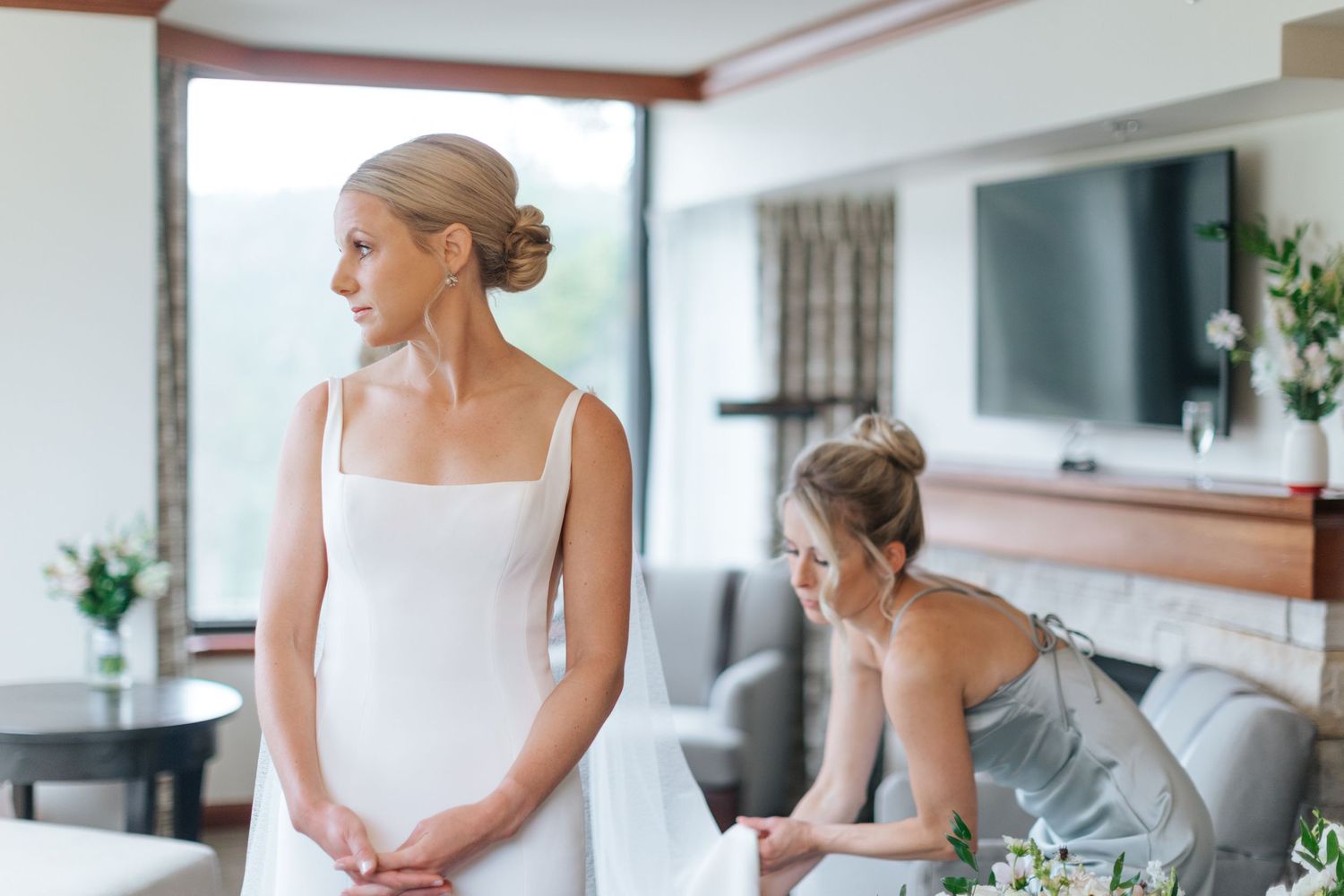 Elegant white wedding dress being fitted and styled in a sunlit room.