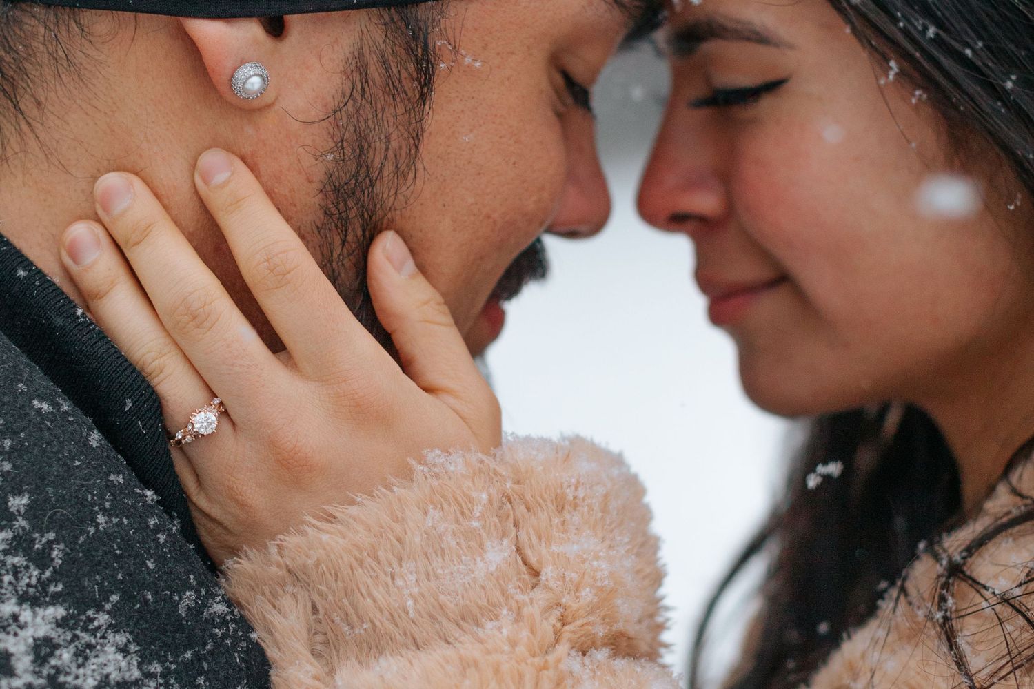 Close-up shot of a couple's intimate moment in the falling snow wearing winter hats.