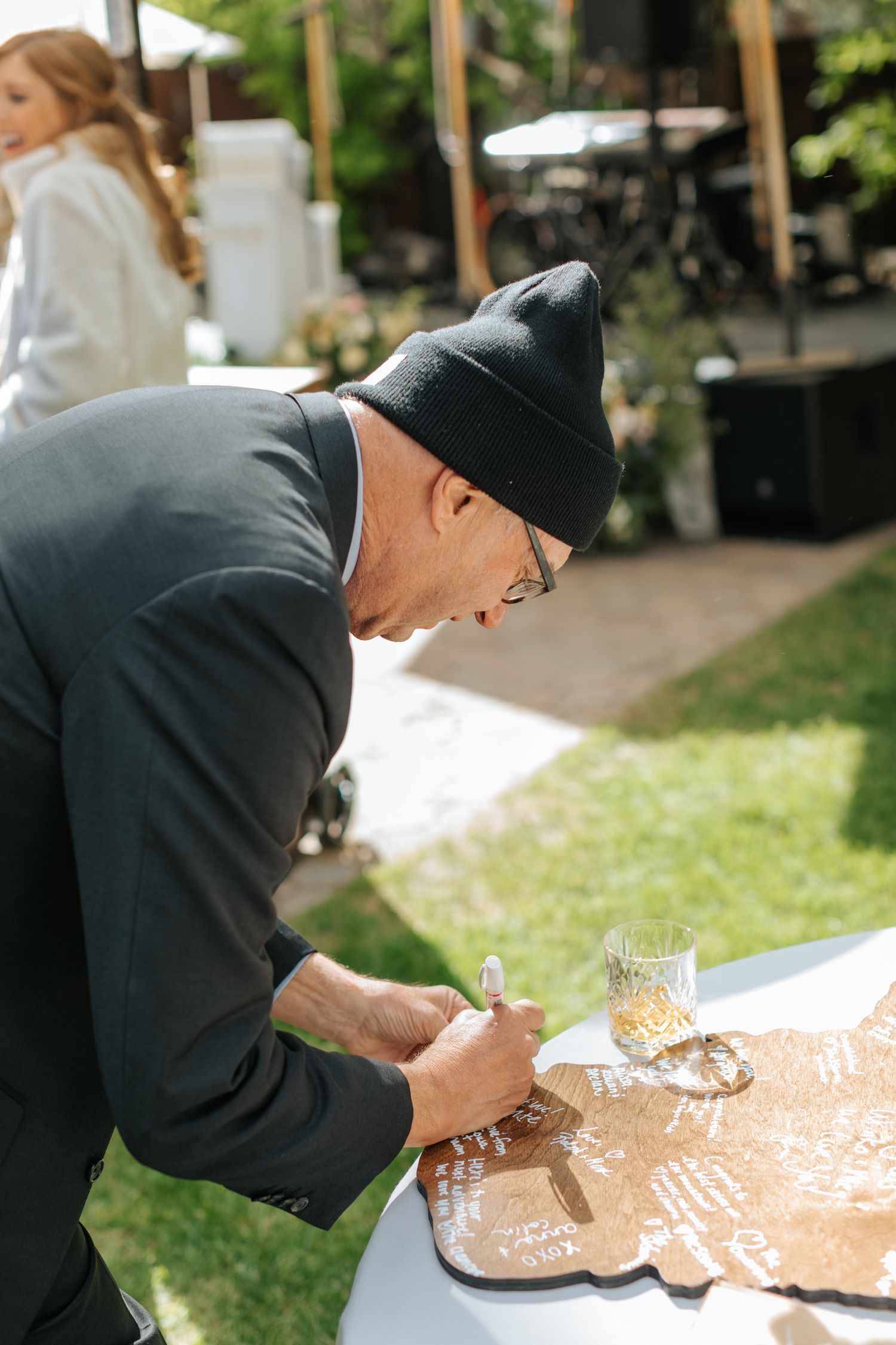 Guest signs wedding guestbook at outdoor reception table.