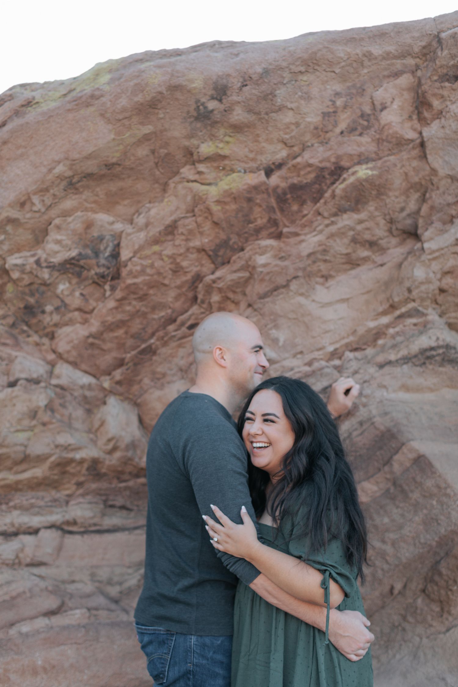 A couple shares joyful laughter while posing against red rock formations.