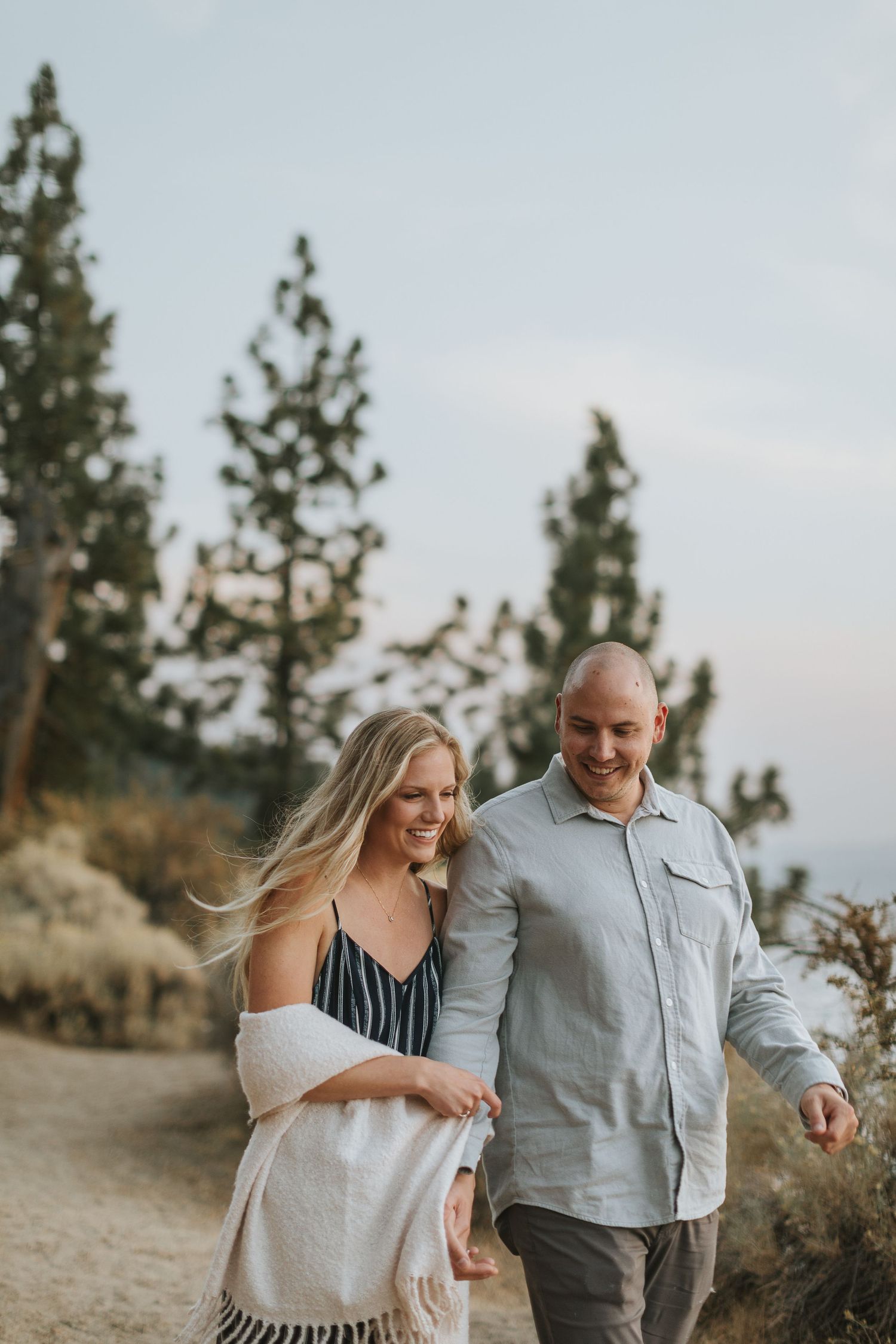 A couple laughs and embraces while walking together on a scenic mountain trail at sunset.