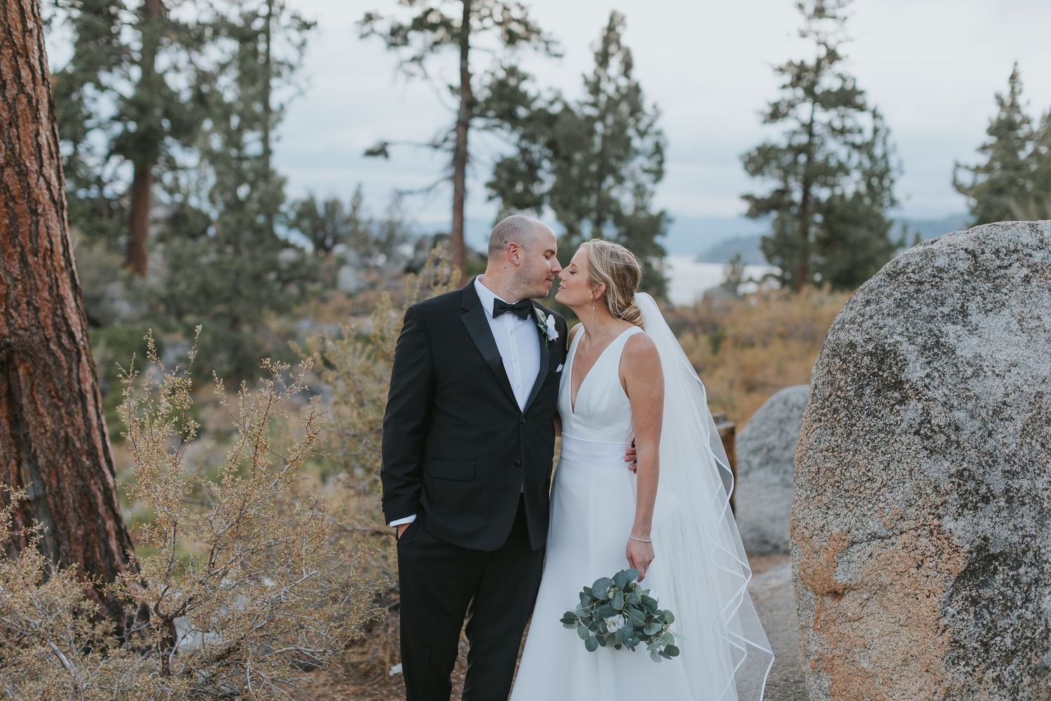 A couple in formal wedding attire walks together on a scenic mountain path.