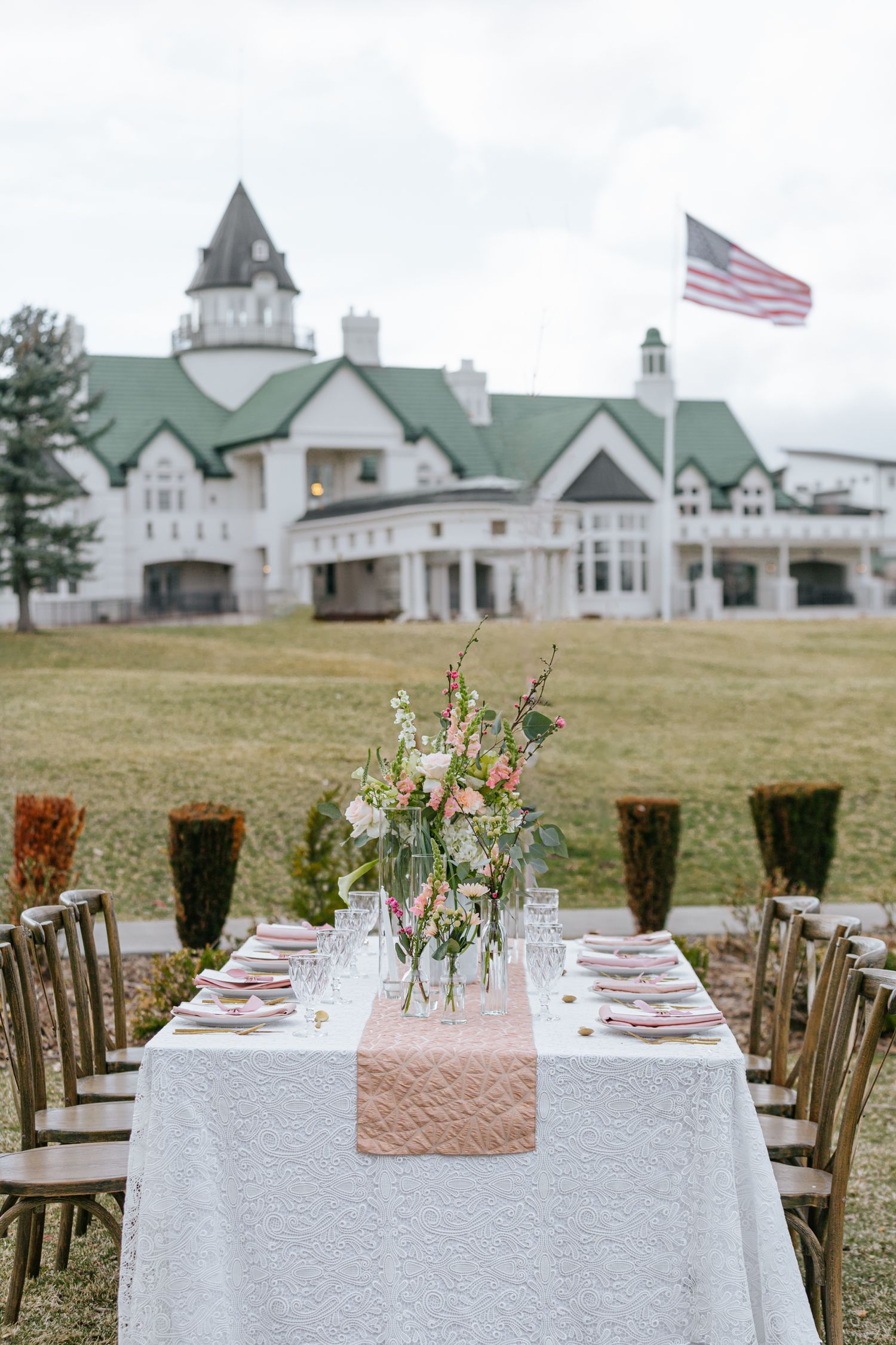 Elegant outdoor wedding reception table with white linens and rustic barn buildings in background.