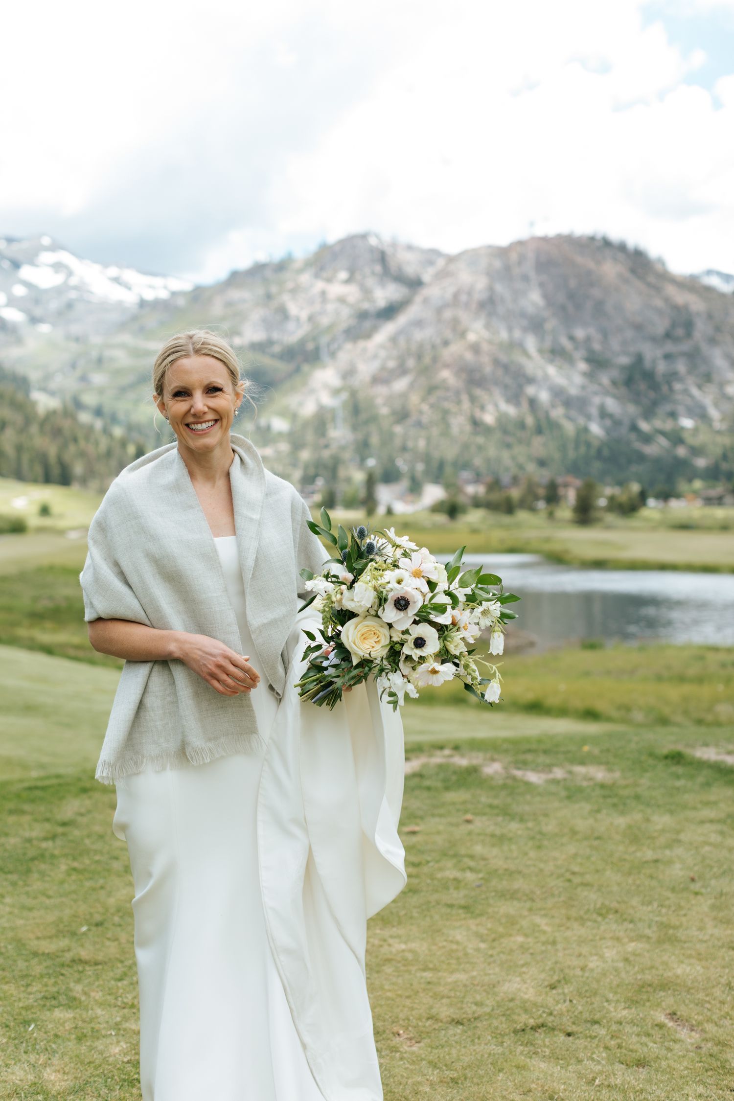 Bride holding a white bouquet against mountain landscape backdrop.