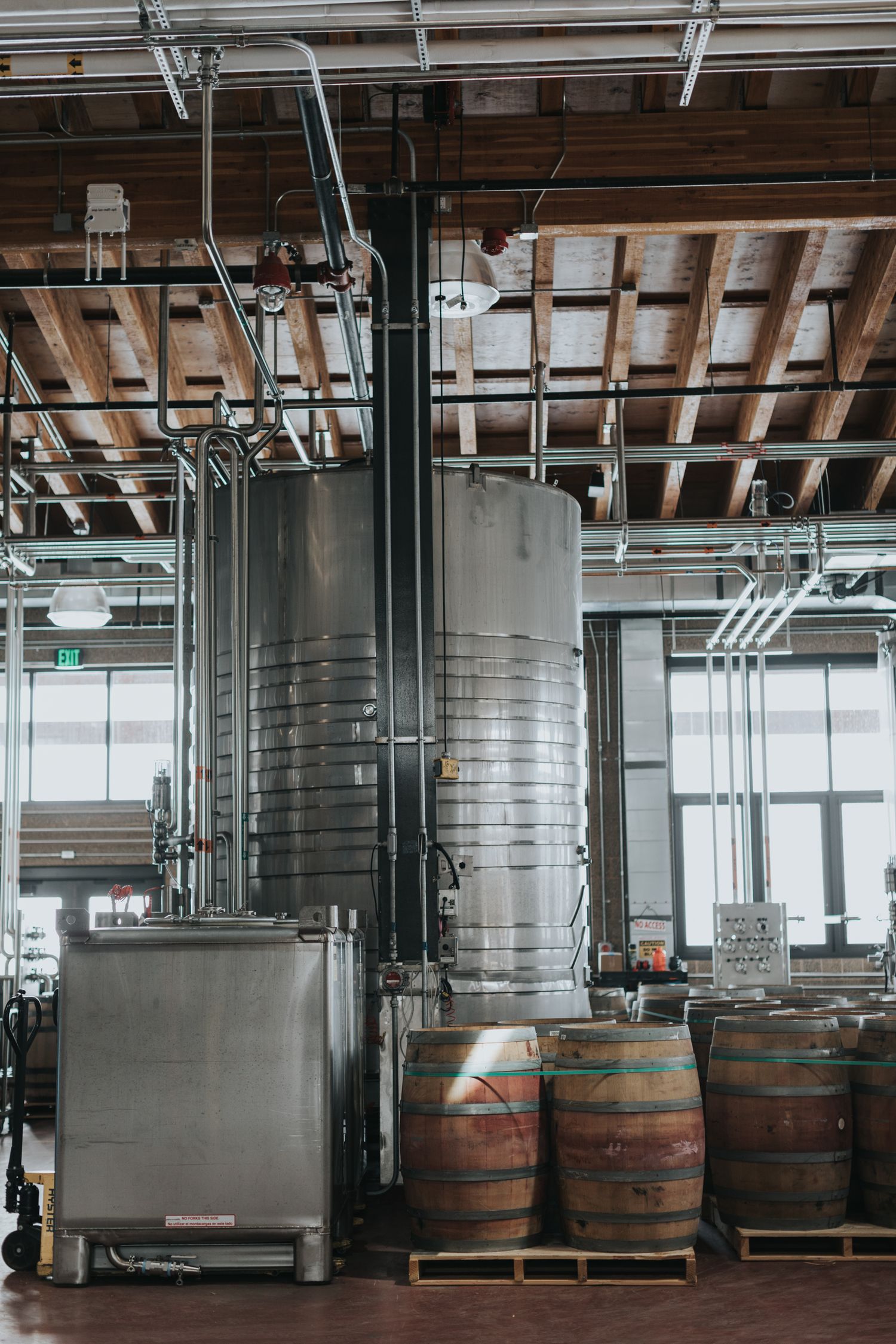 Industrial distillery interior with wooden barrels and stainless steel equipment in a modern facility.