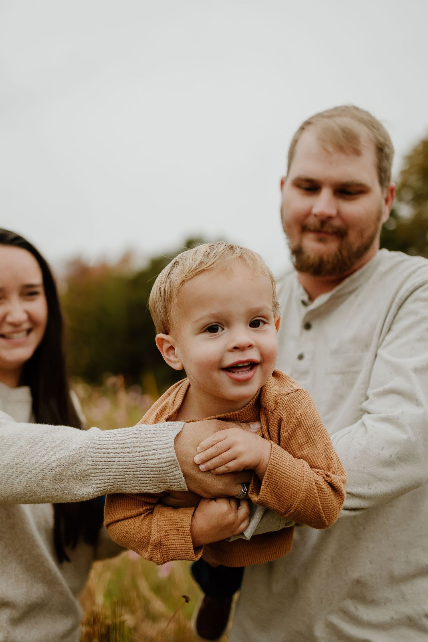 Adorable toddler boy being held by parents in autumn wildflower field.
