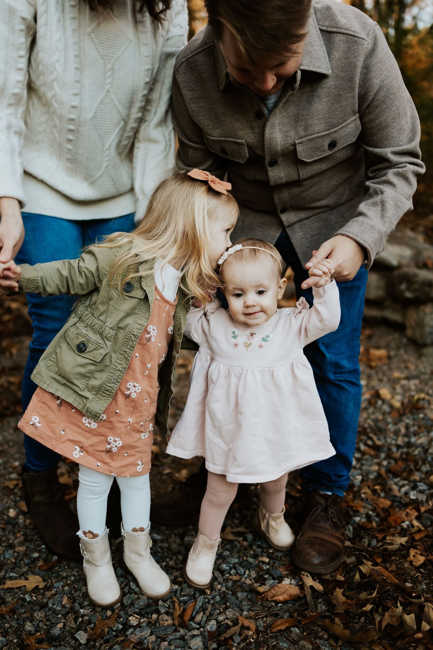 Two toddler sisters in fall outfits holding parents hands during autumn family photo session.