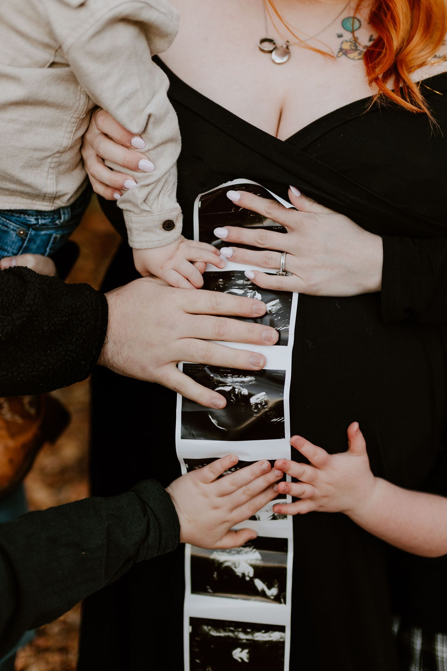 Family holds ultrasound photos against pregnant woman's black dress bump during maternity shoot.