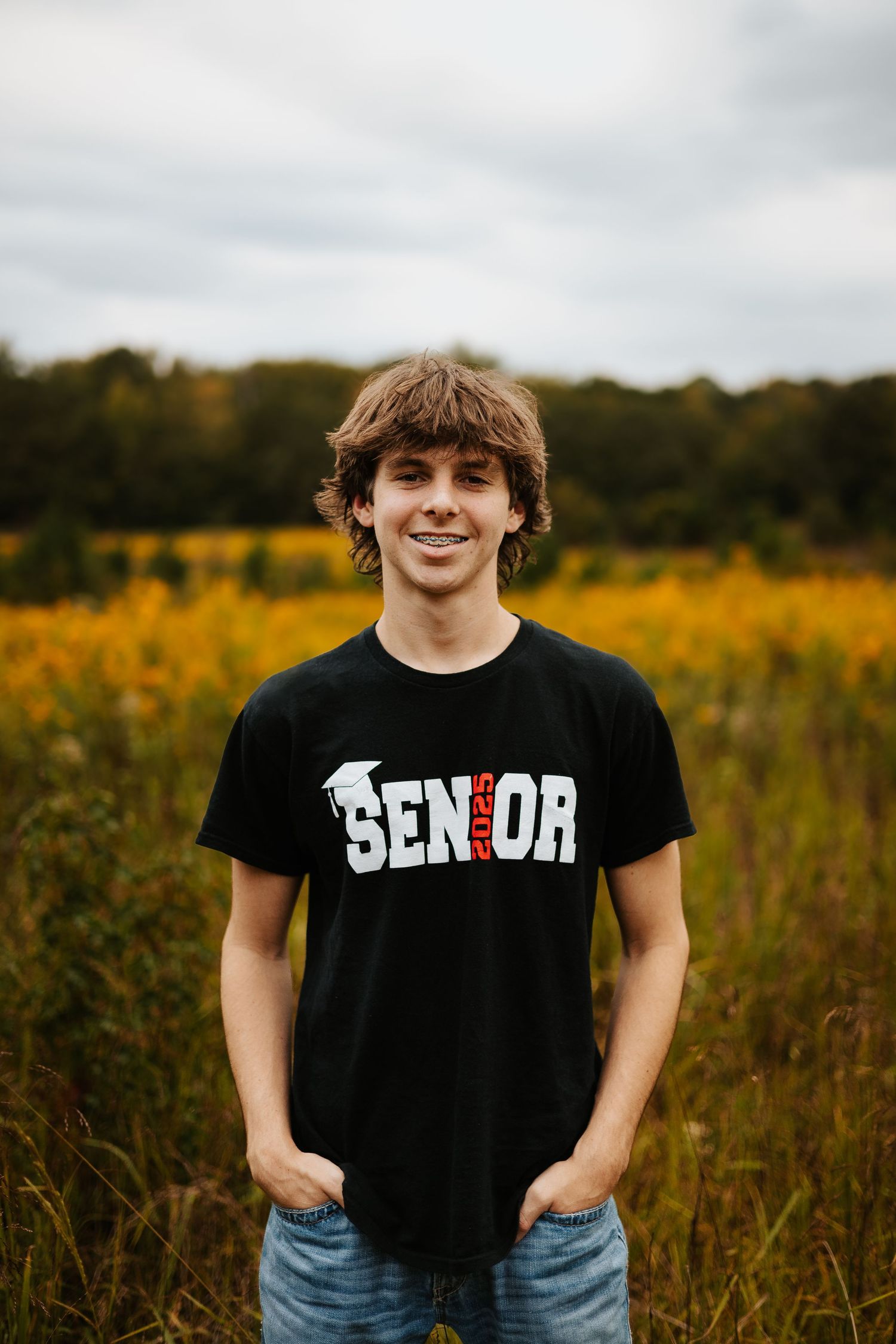 Smiling senior boy in black Senior t-shirt standing in golden autumn wildflower field outdoors.
