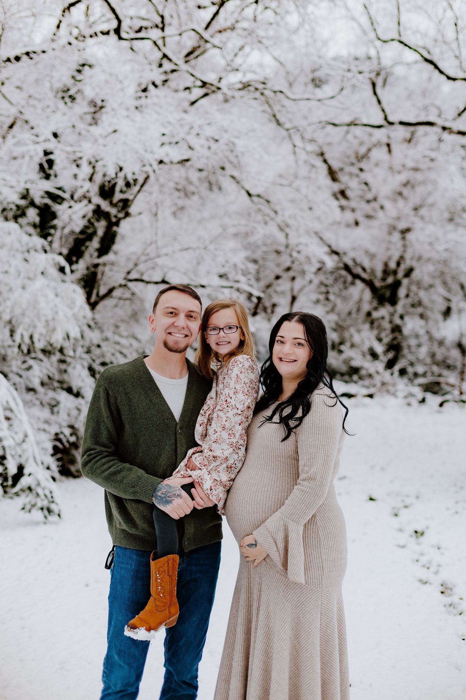 Family maternity portrait with man, daughter, and pregnant woman in snowy winter setting.