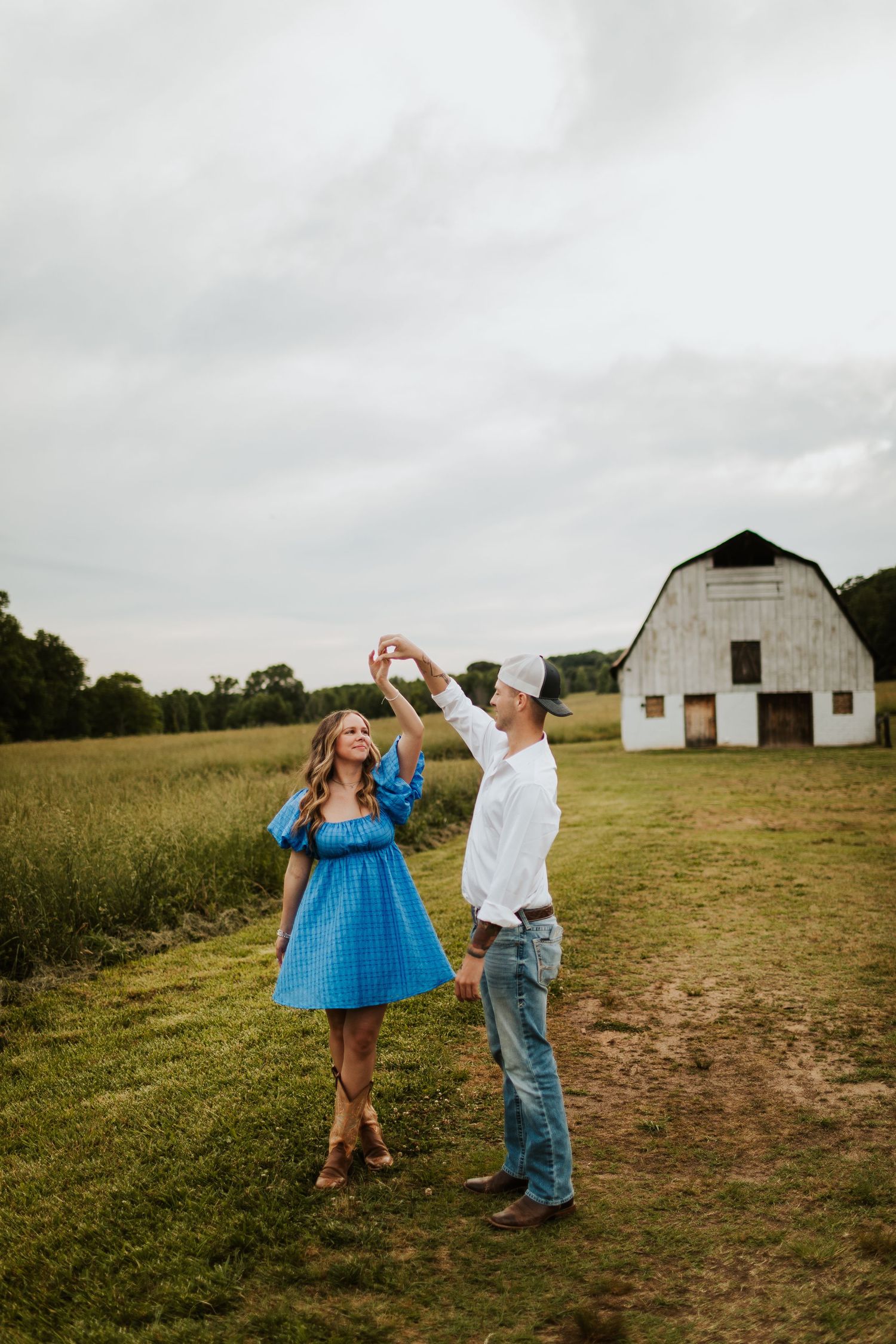 Couple dancing in a green field with a white barn in the background.