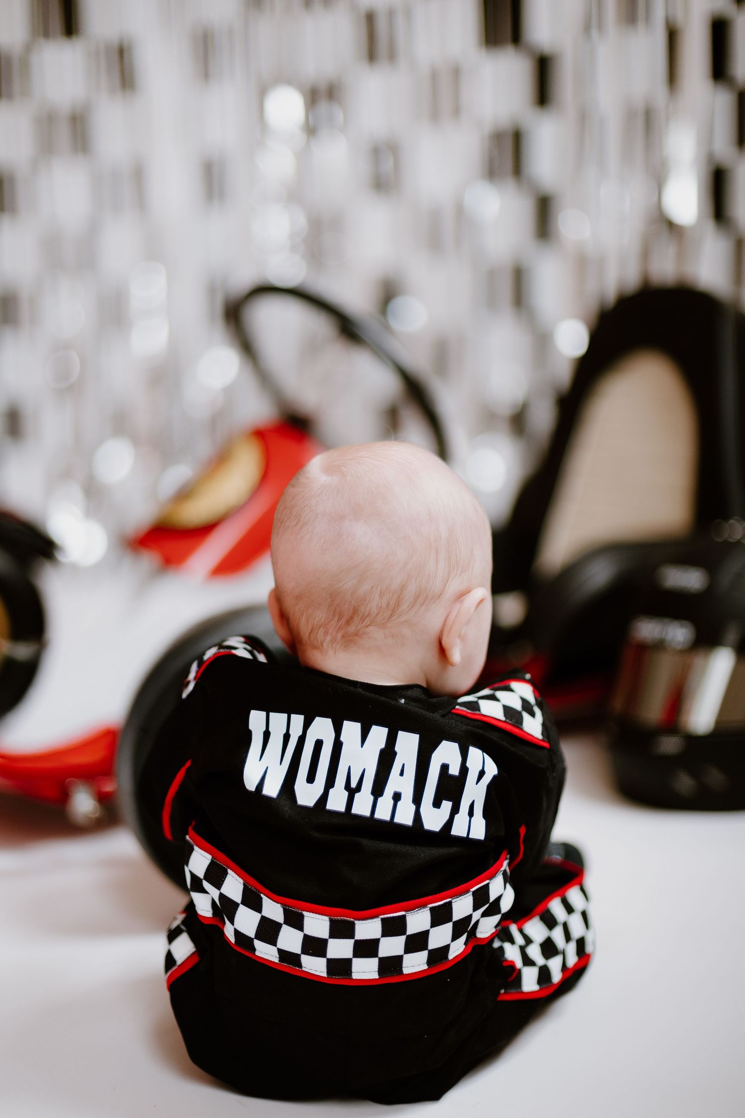 Back view of baby in black racing suit with WOMACK name tag sitting near red go-kart.