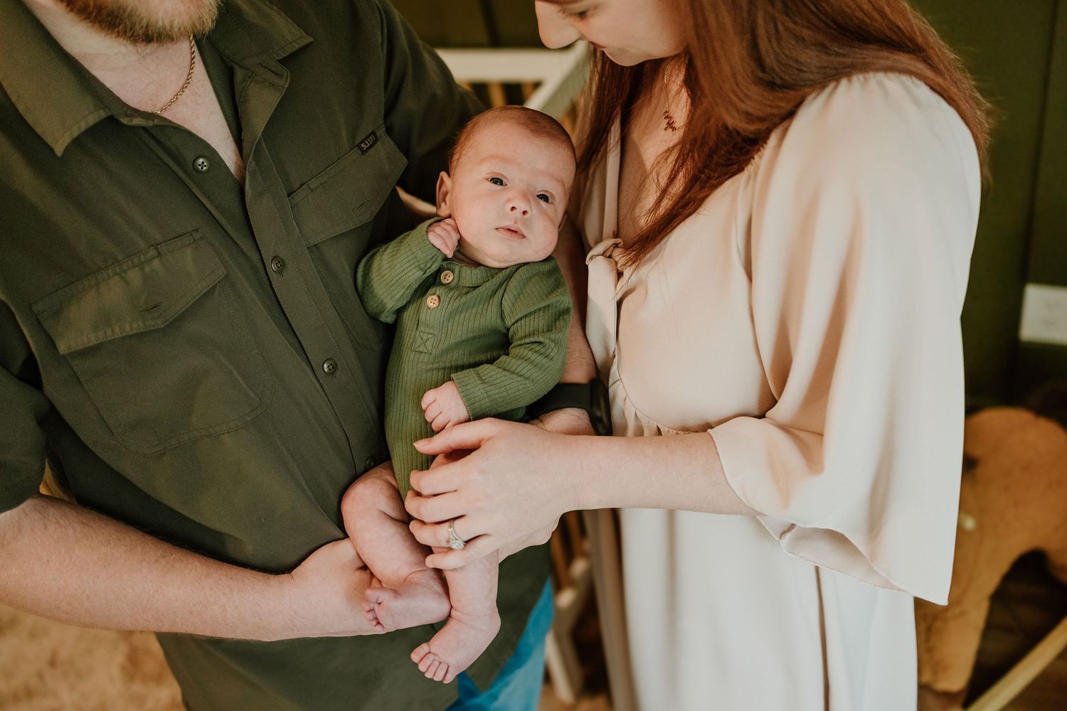 New parents tenderly holding newborn baby dressed in green onesie in nursery.