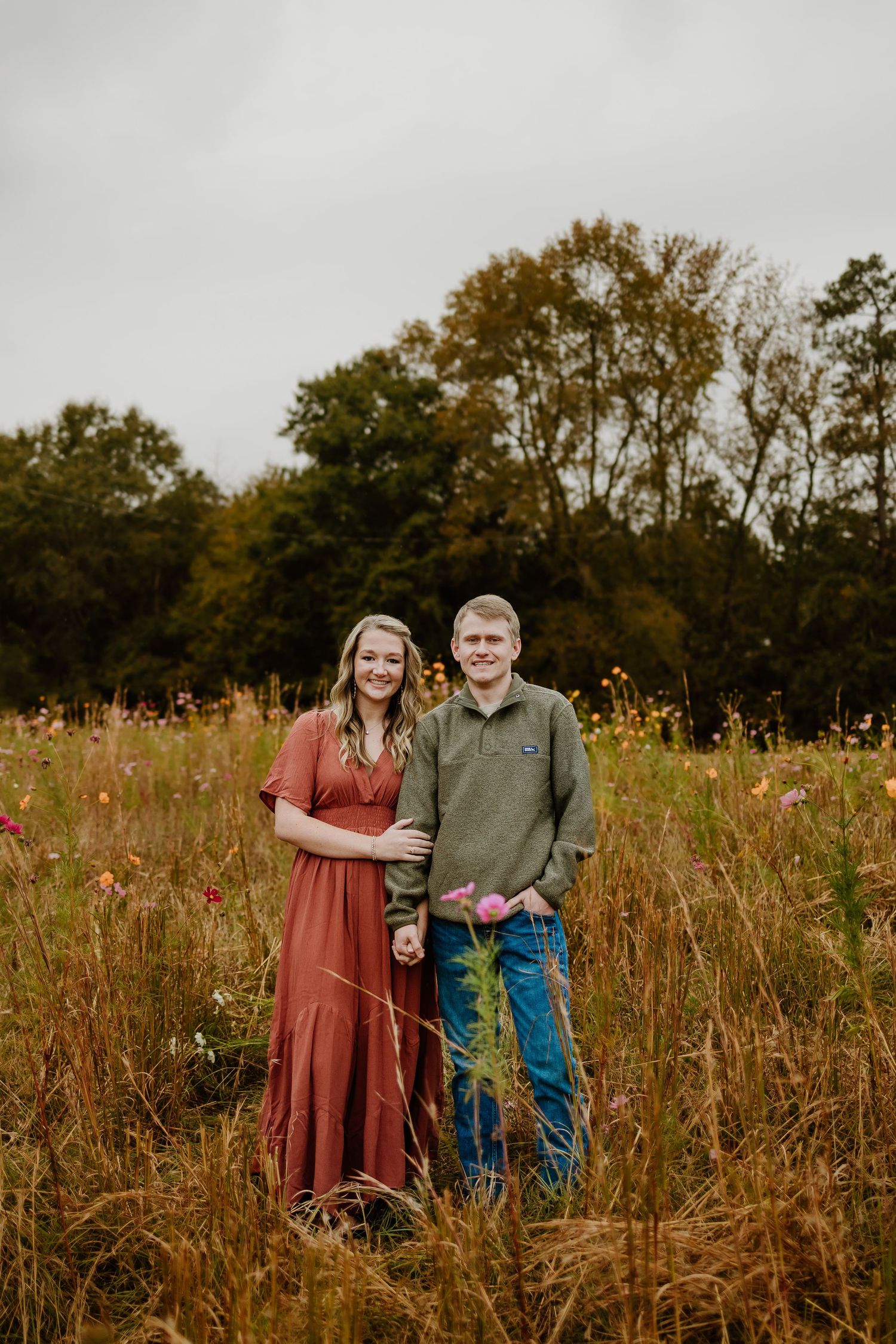 Happy couple standing together in a lush wildflower field on an overcast autumn day.