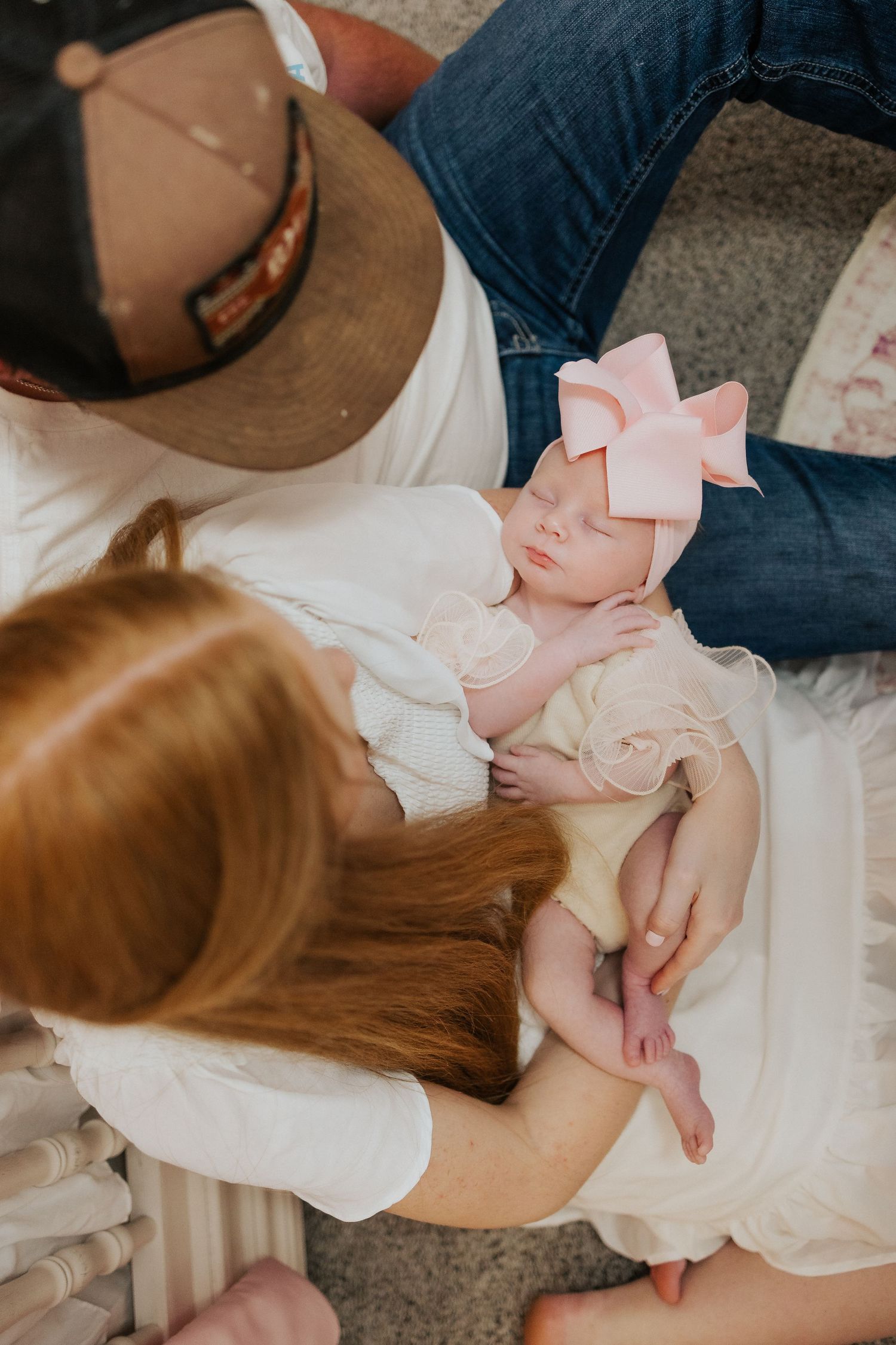 Overhead view of sleeping newborn girl with pink bow held by parents.
