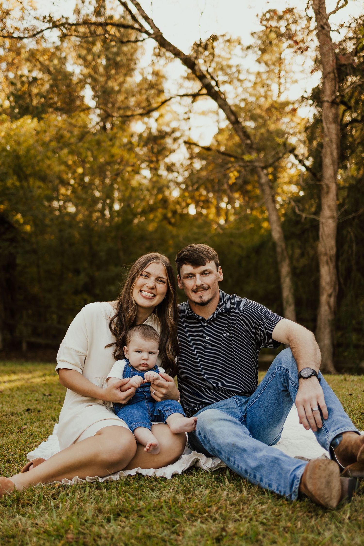 Young family with baby sitting on grass during golden hour fall outdoor portrait session.