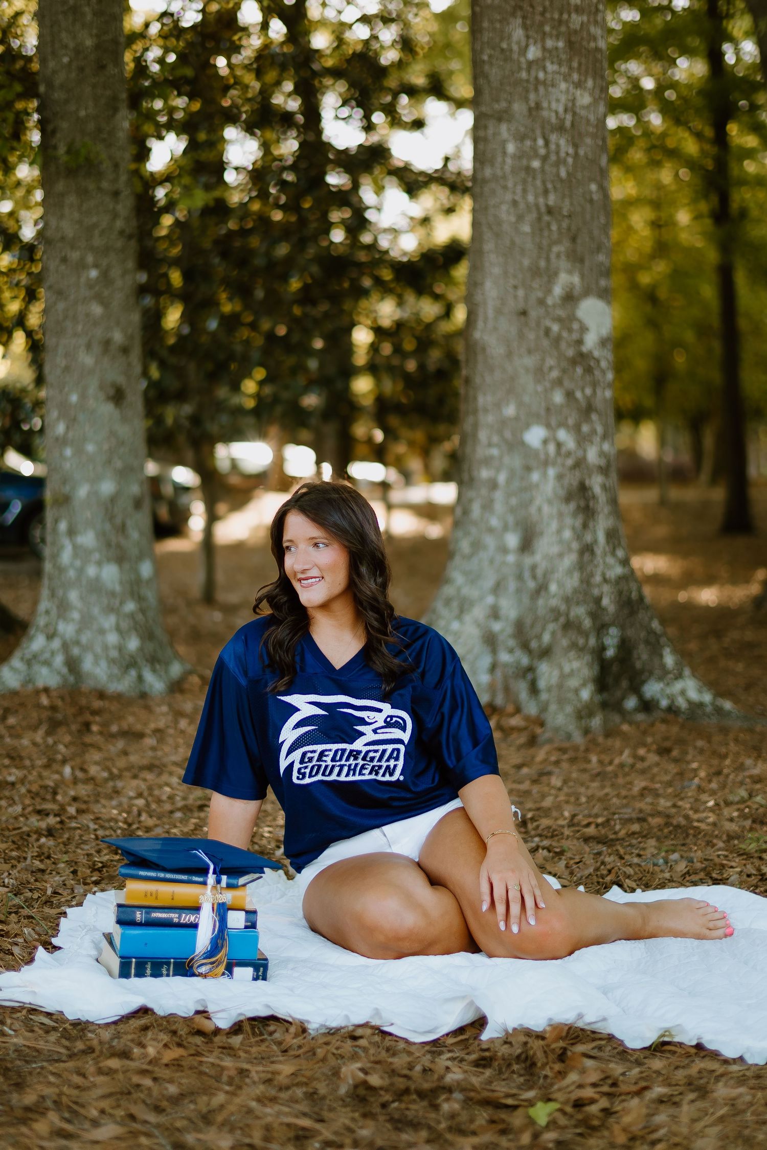 Georgia Southern student in navy jersey sitting on blanket with stacked books under trees.