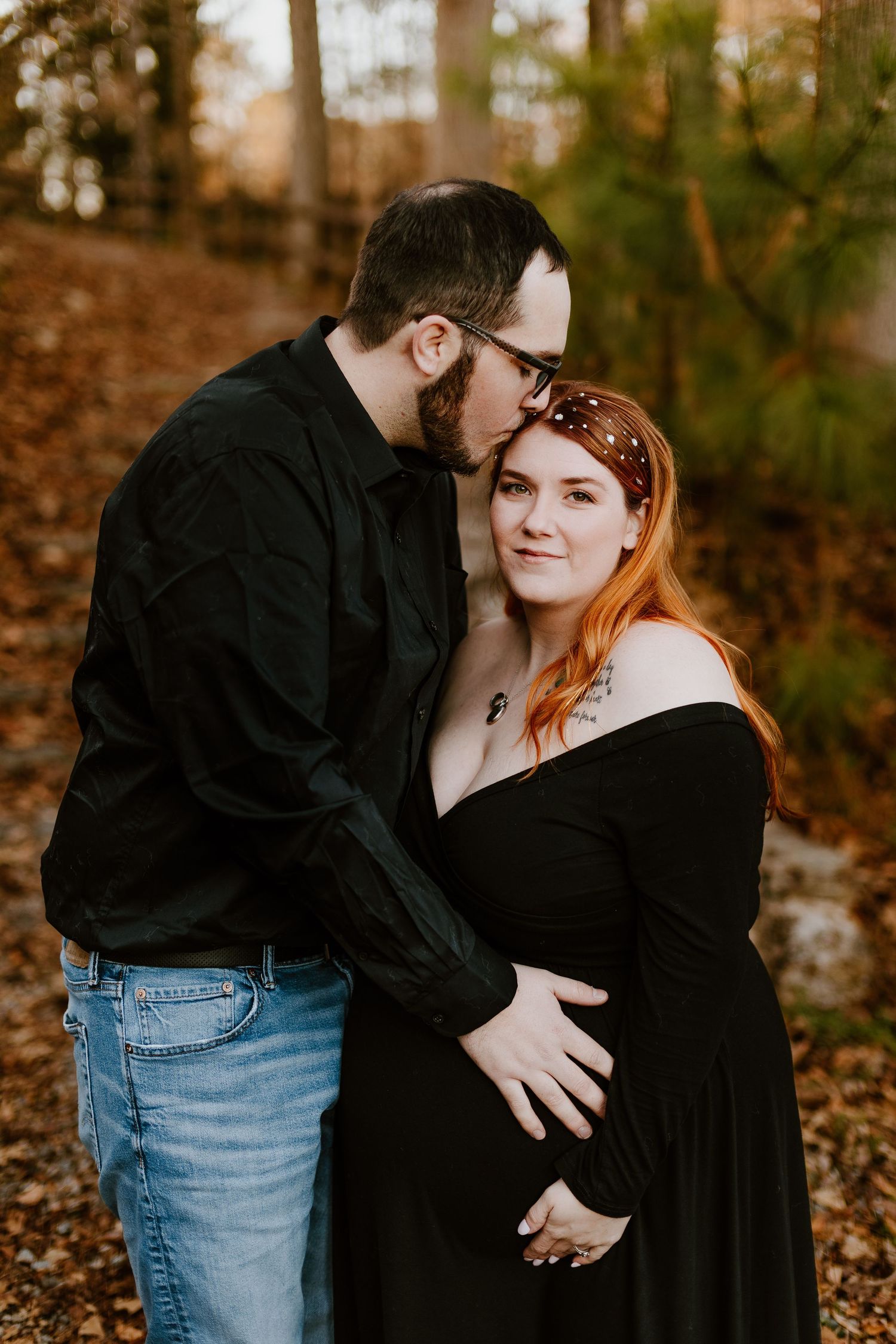 Couple sharing tender moment in autumn forest, man kissing pregnant woman's head.