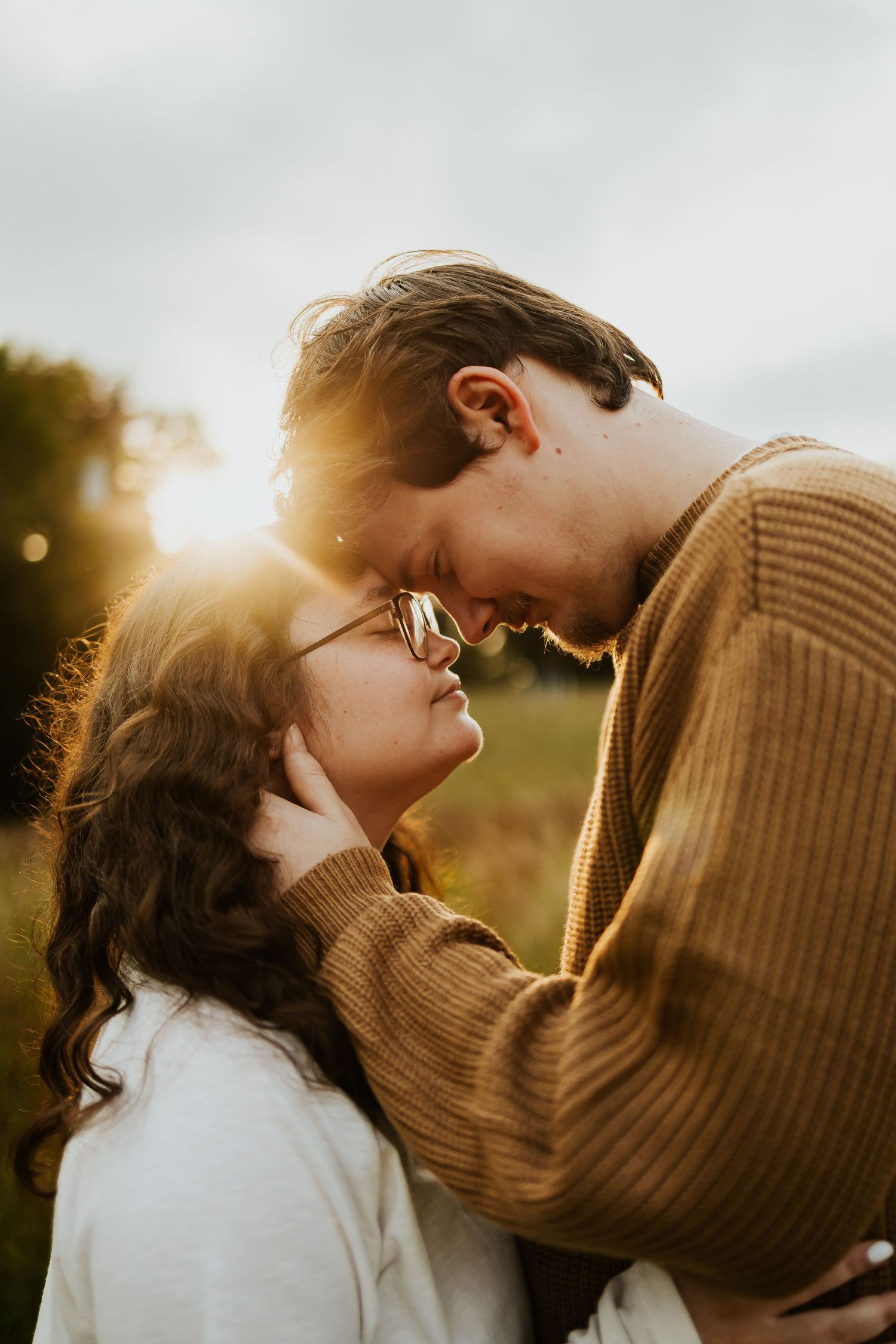 Romantic couple nearly kissing with golden sunset backlight during outdoor engagement photo session.
