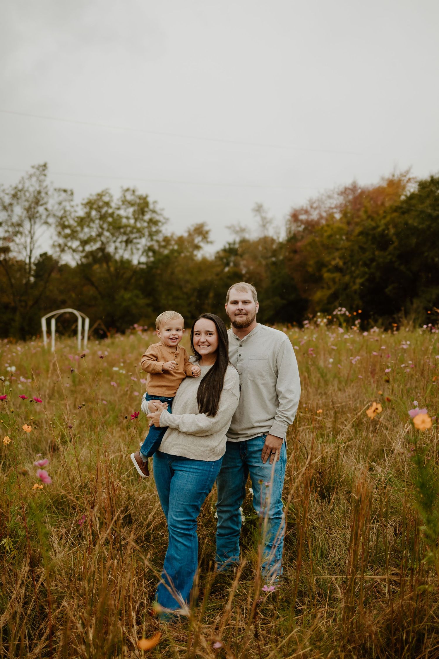Young family of three smiling together in colorful wildflower meadow in autumn.