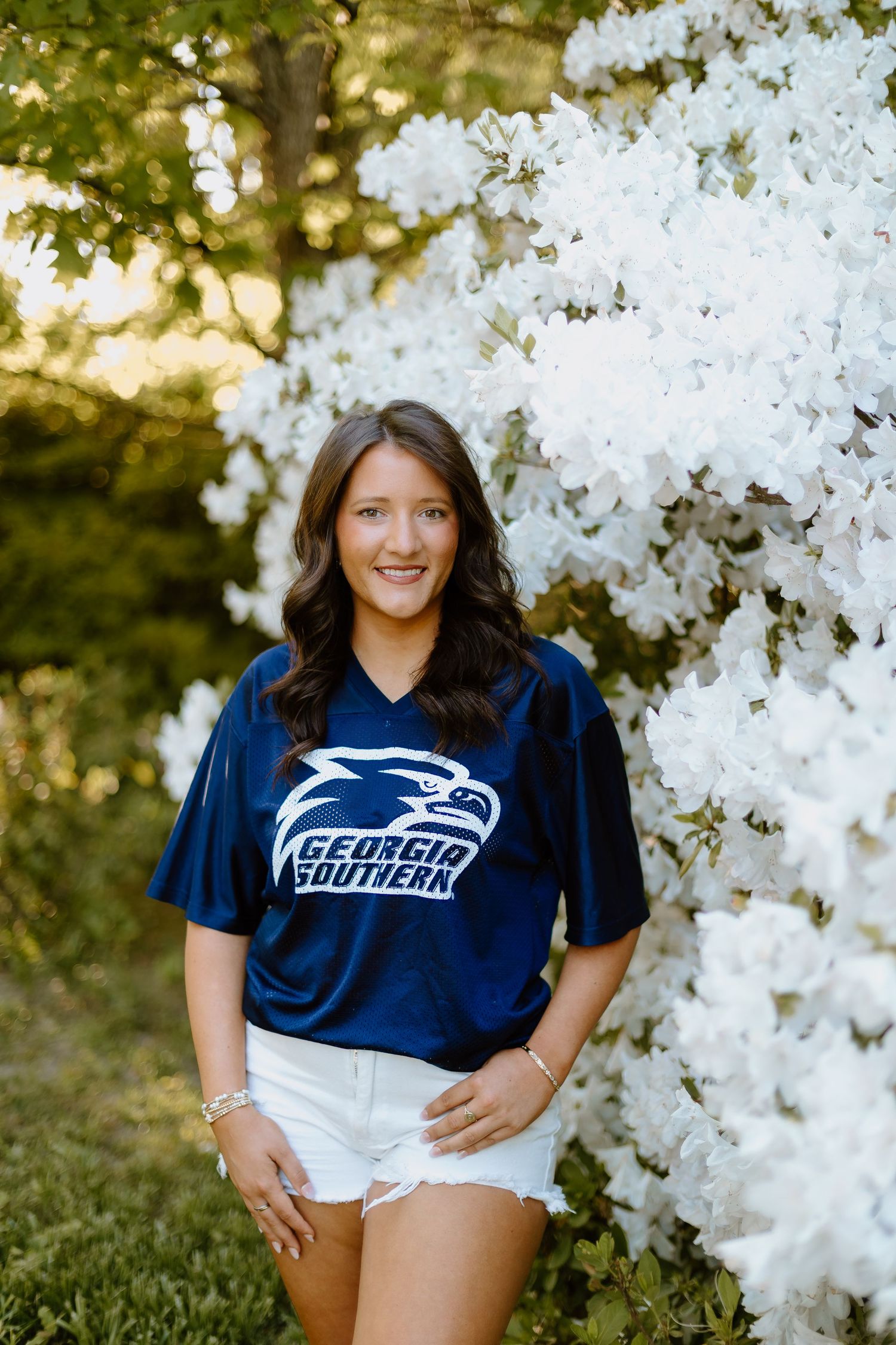 Woman in Georgia Southern navy jersey posing in front of blooming white flower bushes.