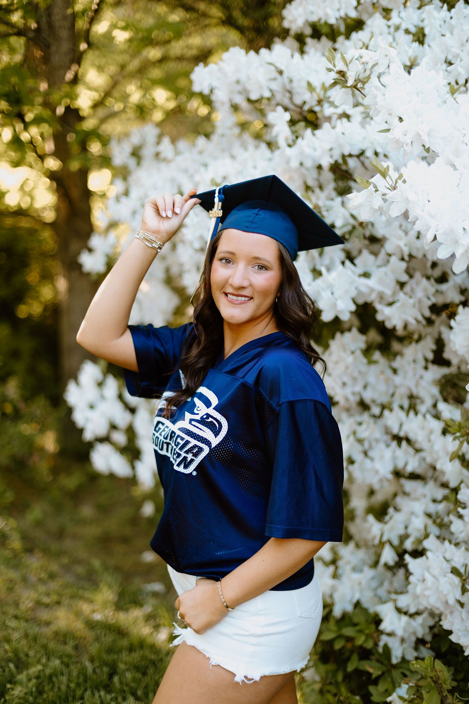 Graduate in Georgia Southern jersey and navy cap posing near white flowering bushes.