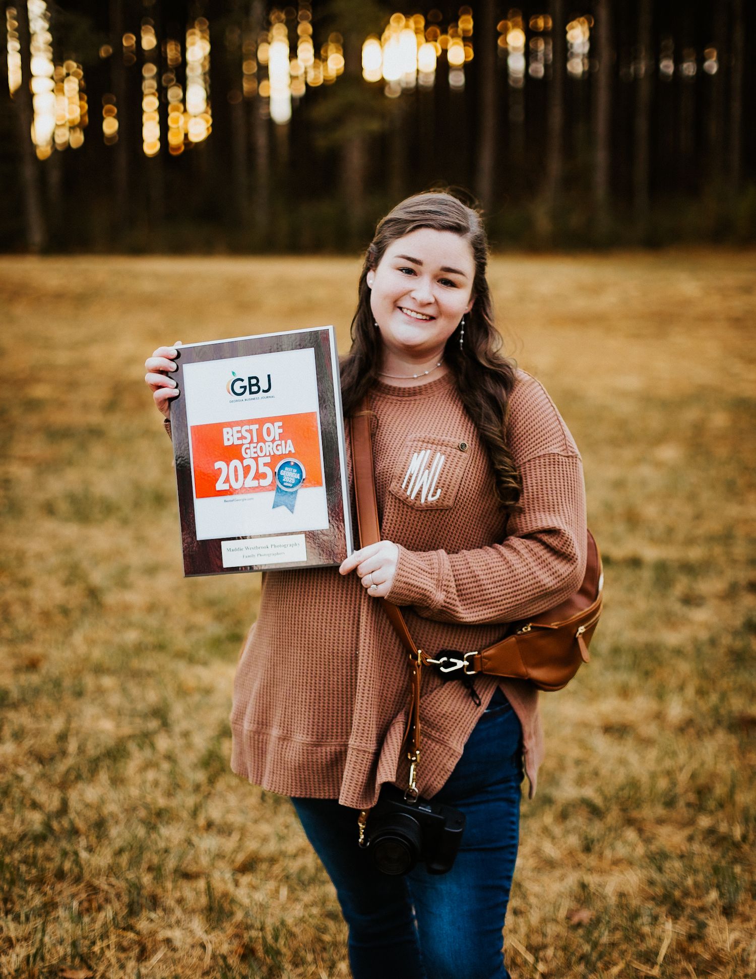 Smiling woman holding a Best of Georgia 2025 GBJ award in a golden sunlit open field.