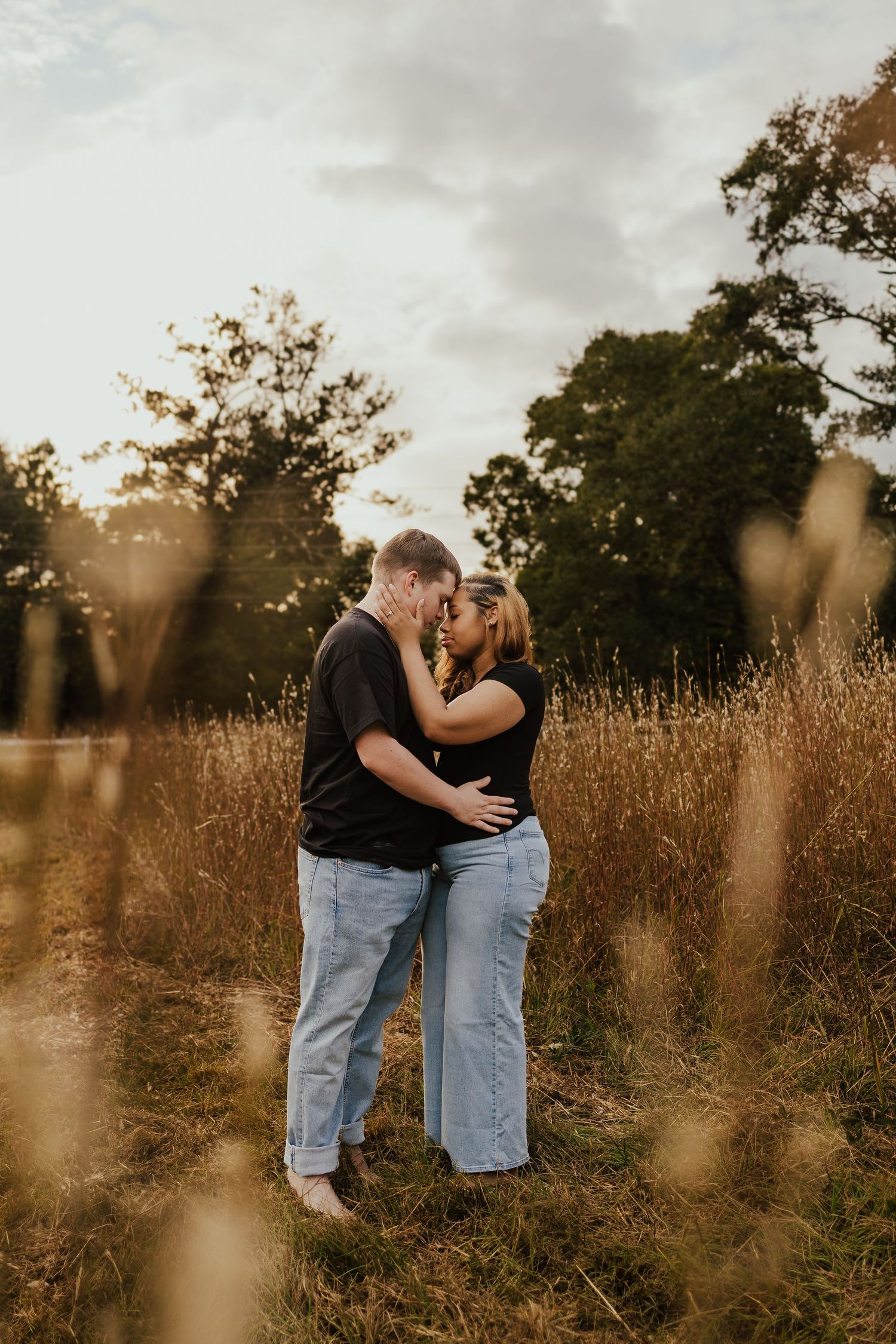 Couple sharing a kiss in a golden grass field during a glowing sunset.
