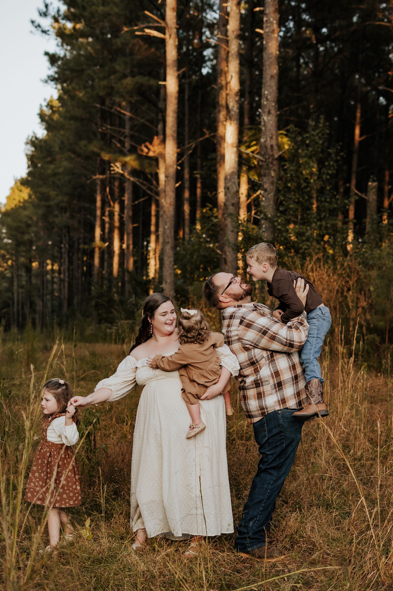 Family of five enjoys a playful moment together in a golden sunlit pine forest at sunset.