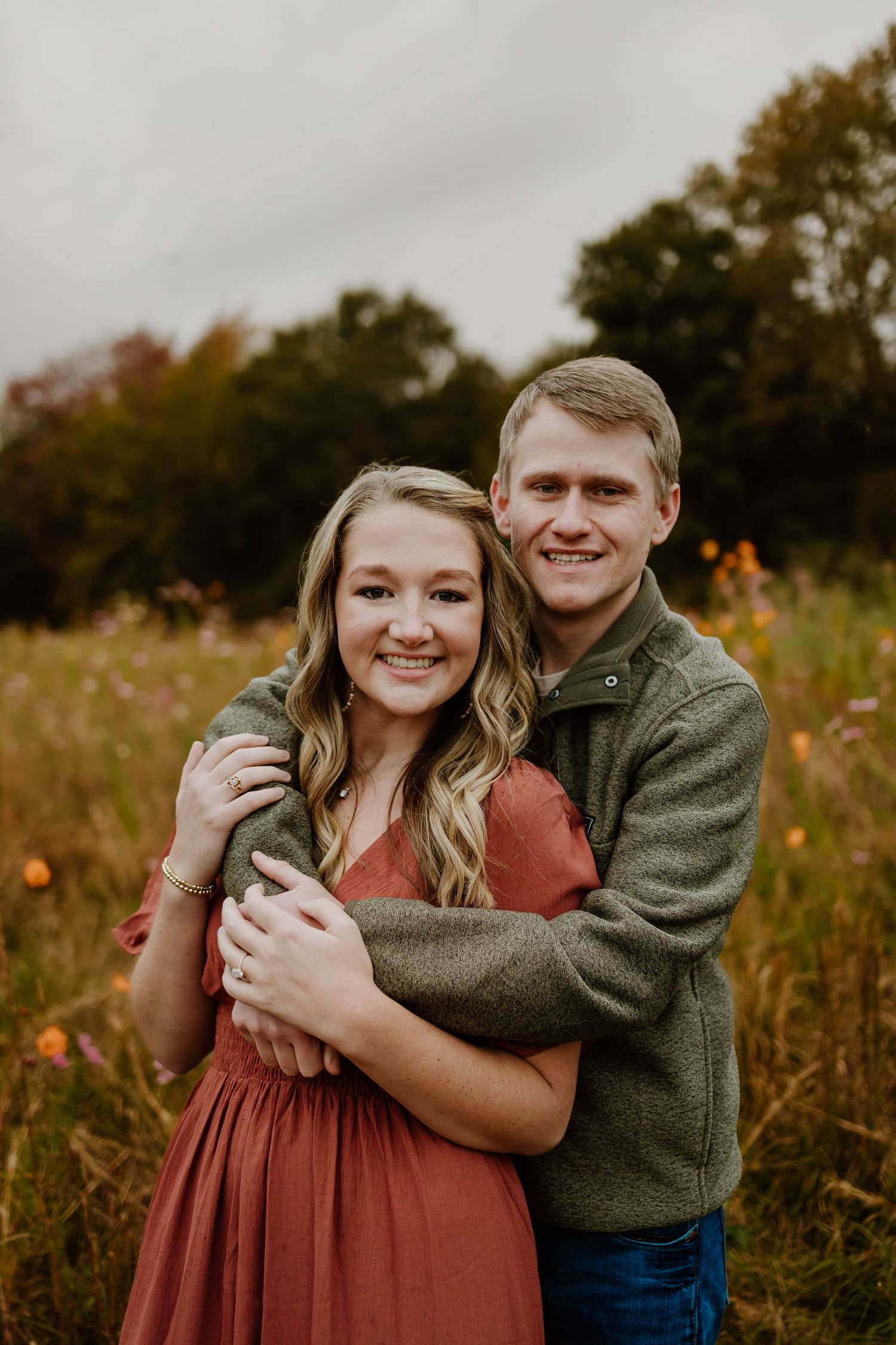 Smiling couple embracing in a wildflower meadow during an outdoor engagement session.