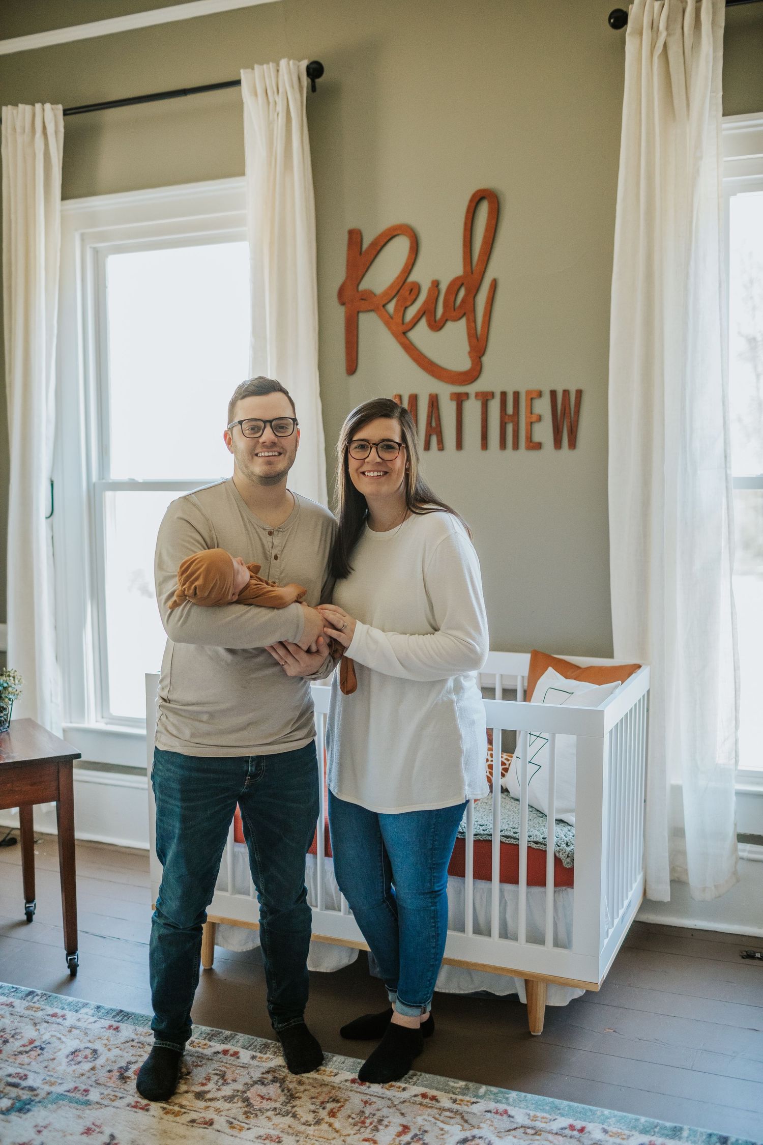 Proud parents holding newborn in nursery with Reid Matthew wooden name sign.