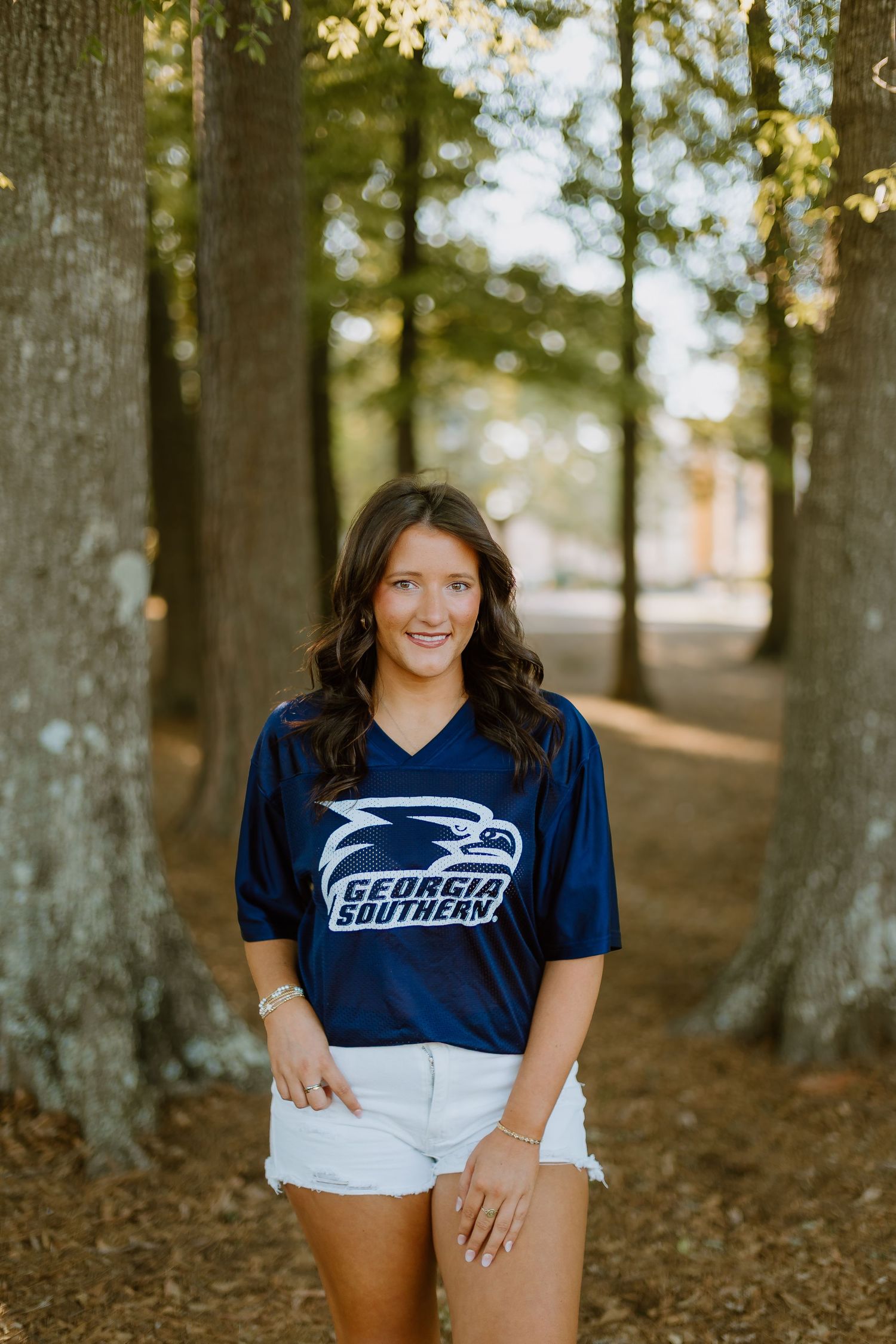 Smiling woman in Georgia Southern Eagles navy jersey standing between trees on campus.