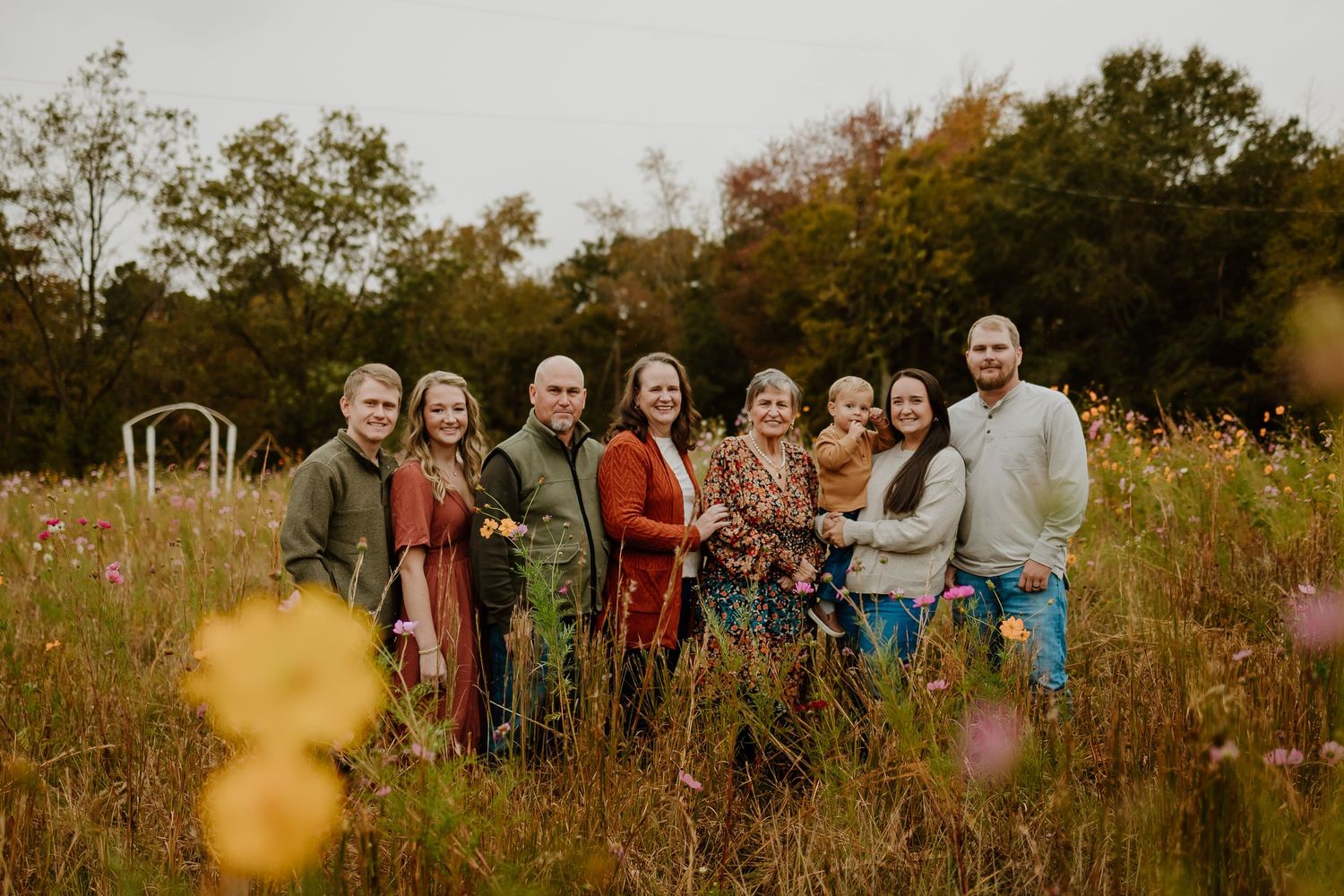 Extended family of eight poses together in a vibrant wildflower meadow during fall photo session.